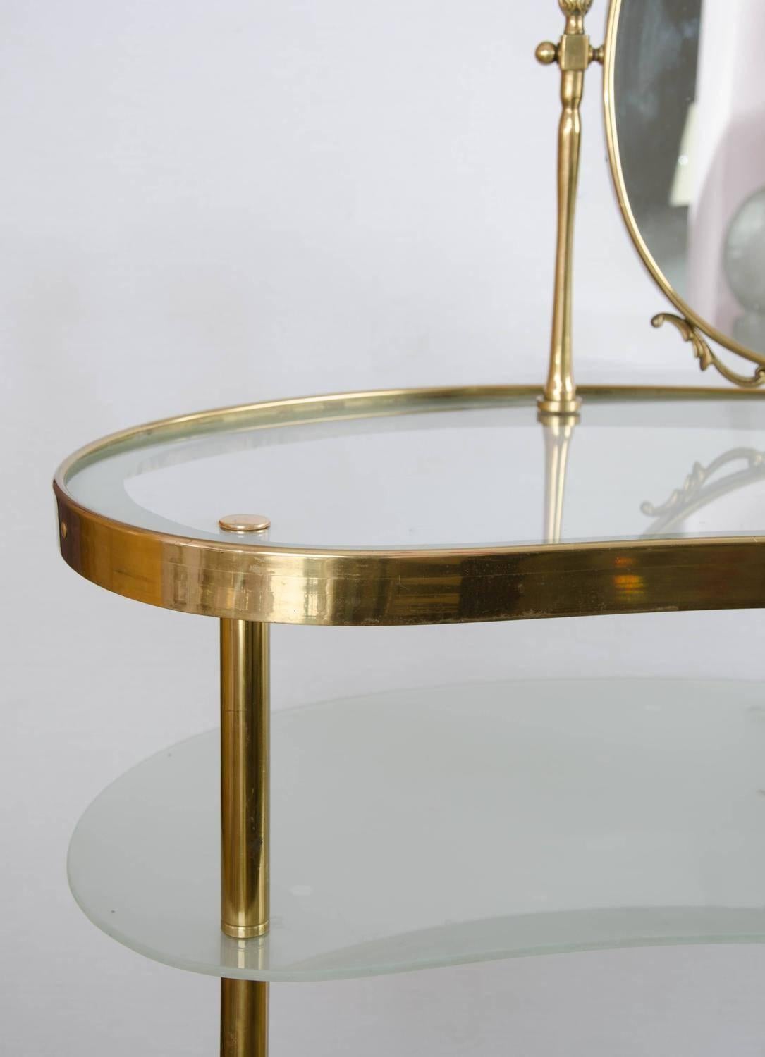 Two-tiered 1950s dressing table with integral oval mirror surrounded by decorative brass detailing. The lower shelf of etched glass with polka dot patterning has a fitted light to add a touch of glamour.