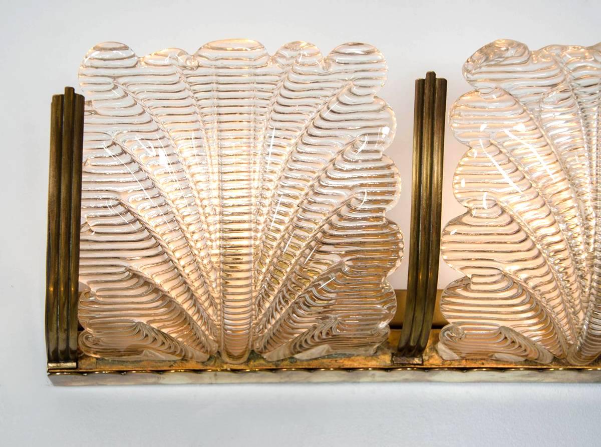 Elegant wall lights in brass and Murano glass, each made up of four stylised glass 'leaves' supported by a brass bracket, with fluted brass finials between each leaf and on the sides.
