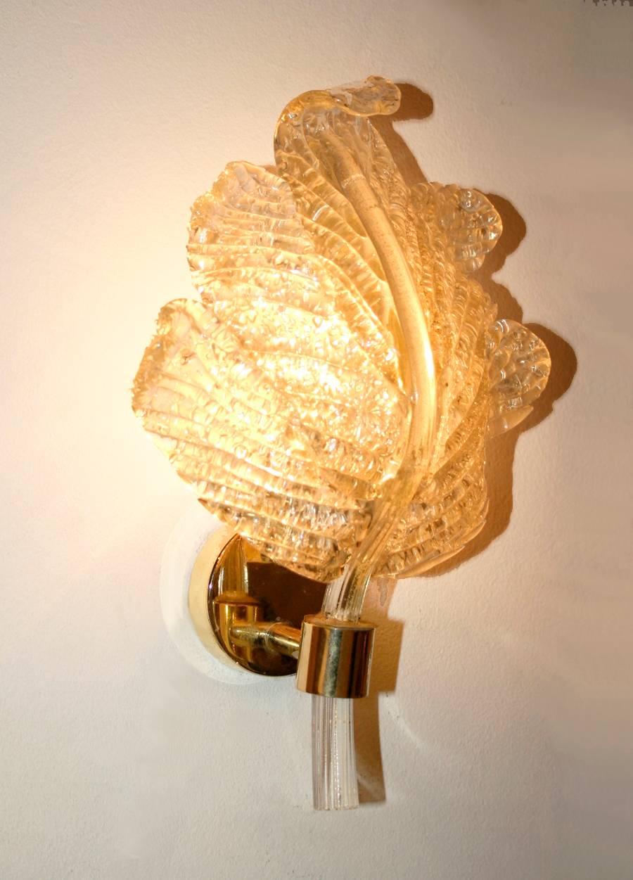 Elegant pair of wall lights in the form of clear glass leaves mounted on brass holders creating a sparkly and atmospheric light.