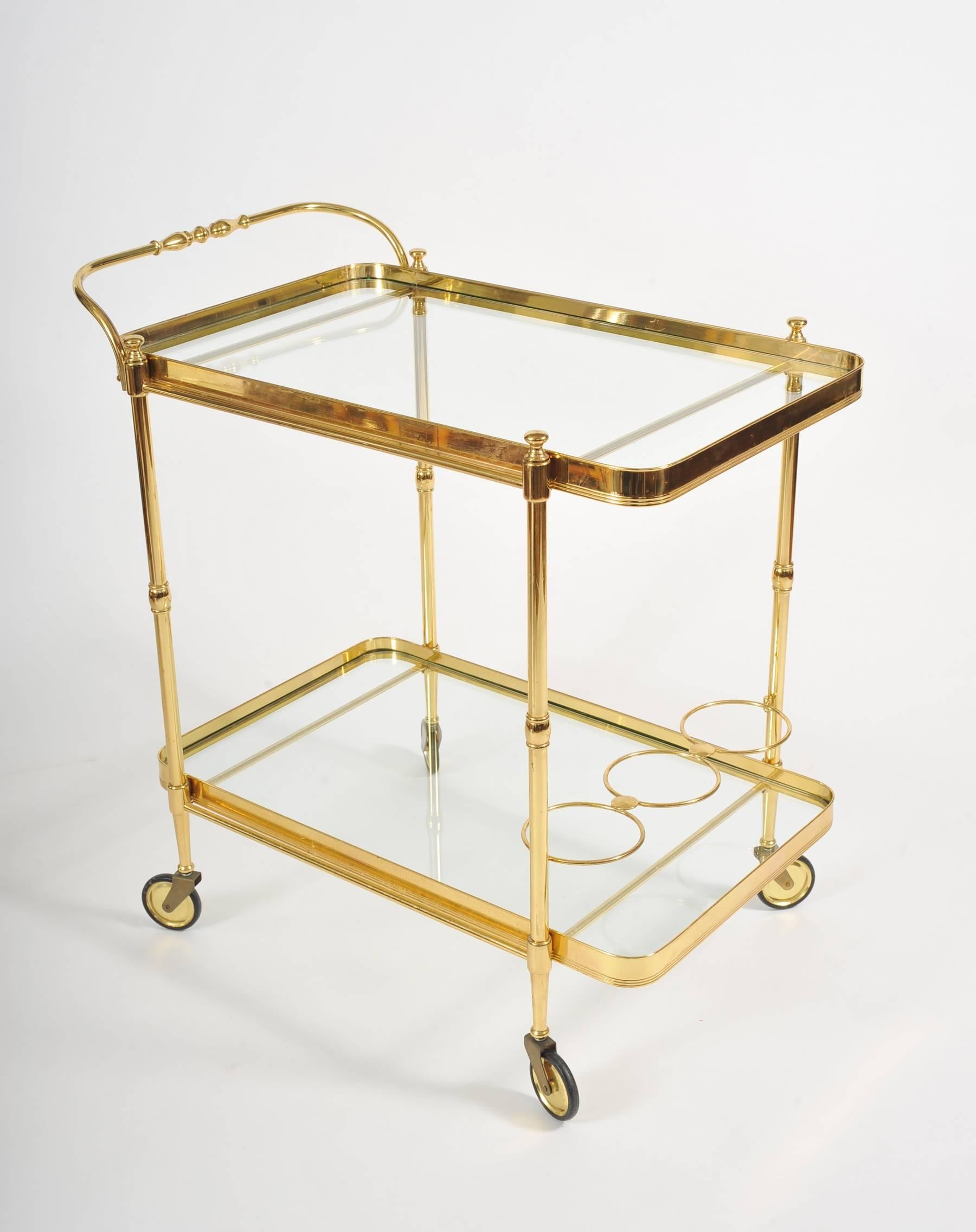 Brass drinks trolley with two glass shelves, curved corners and elegant handle. Brass holders to store bottles.