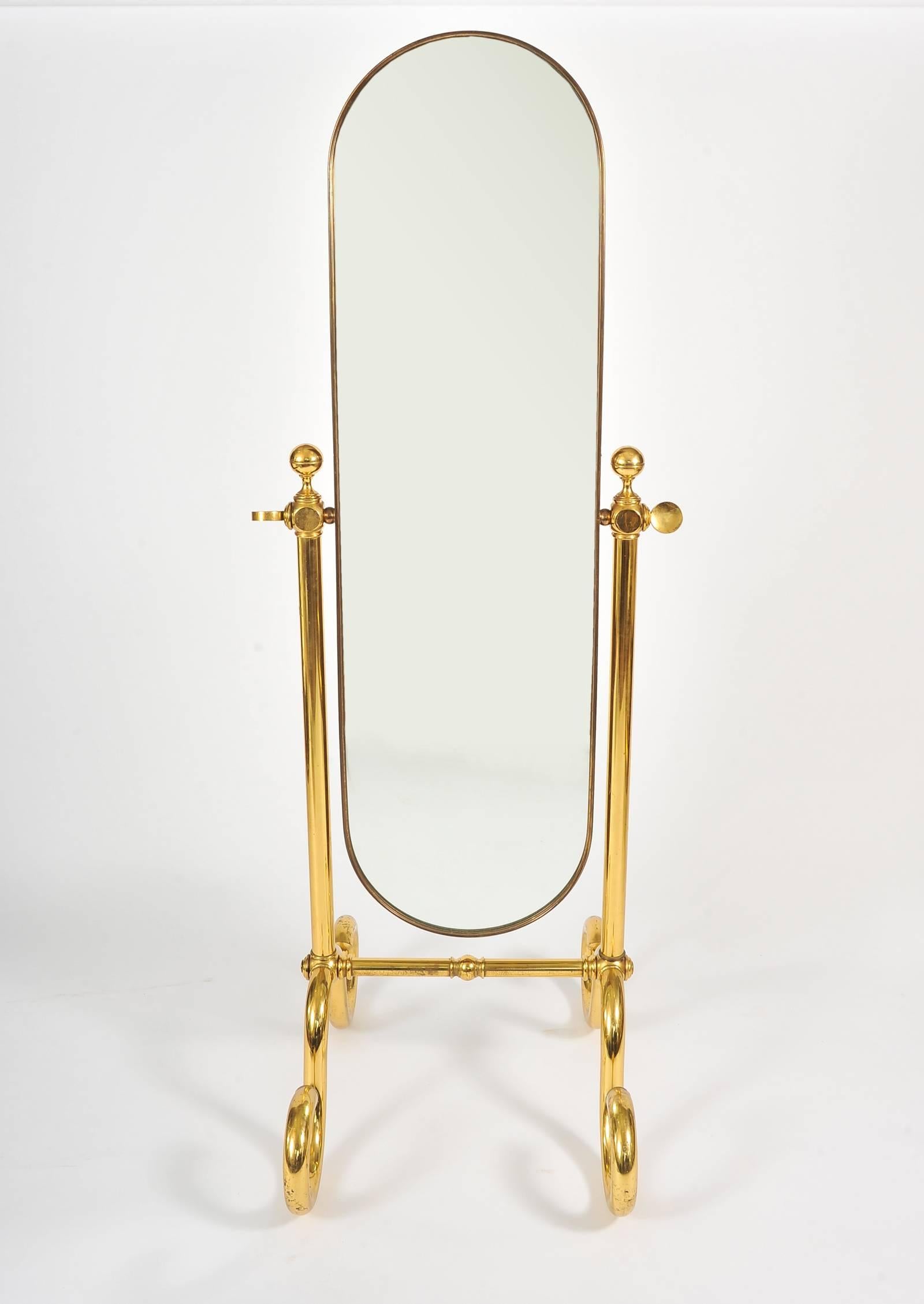 Handsome freestanding mirror. Curved brass frame supported by two brass columns with substantial twirly brass feet. The mirror is balanced so, when angled, holds position.