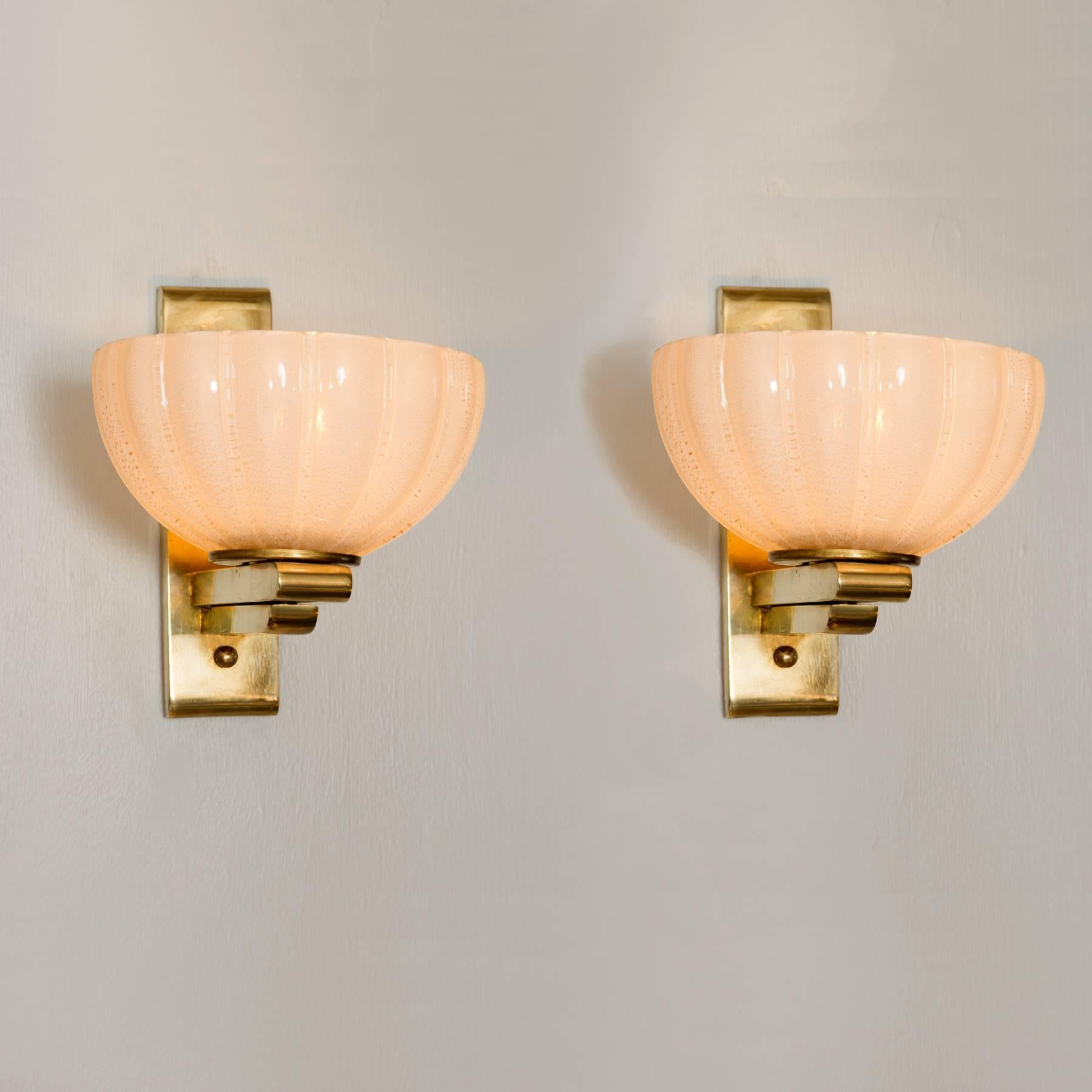 Chic wall lights each with a brass bracket holding a delicate ribbed cup of aerated white glass, can be sold individually.