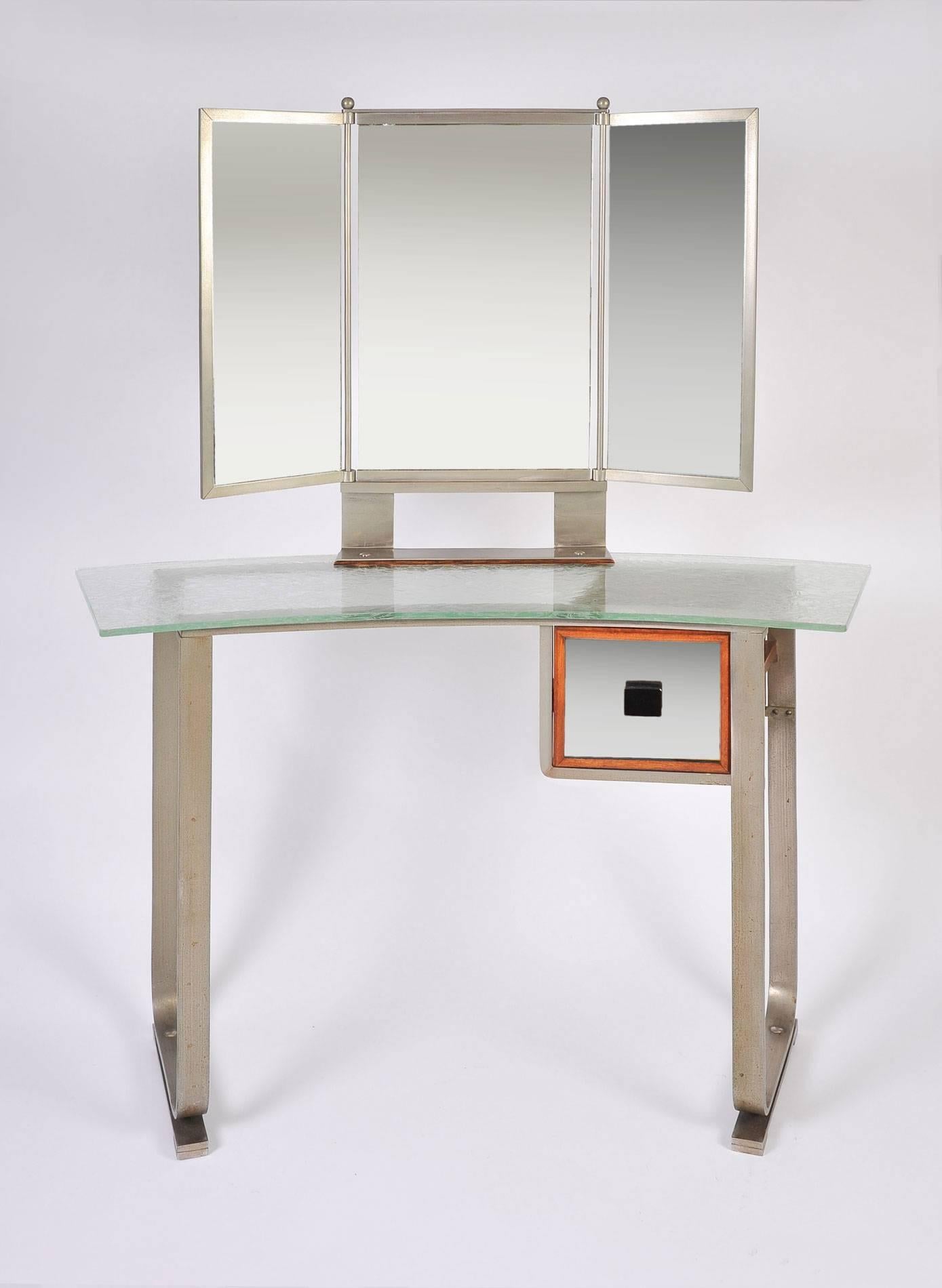 Rare chrome and pale green textured glass dressing table. The triptych mirror stands on wide chrome supports and is surrounded in chrome. Single glass drawer has wooden trim.