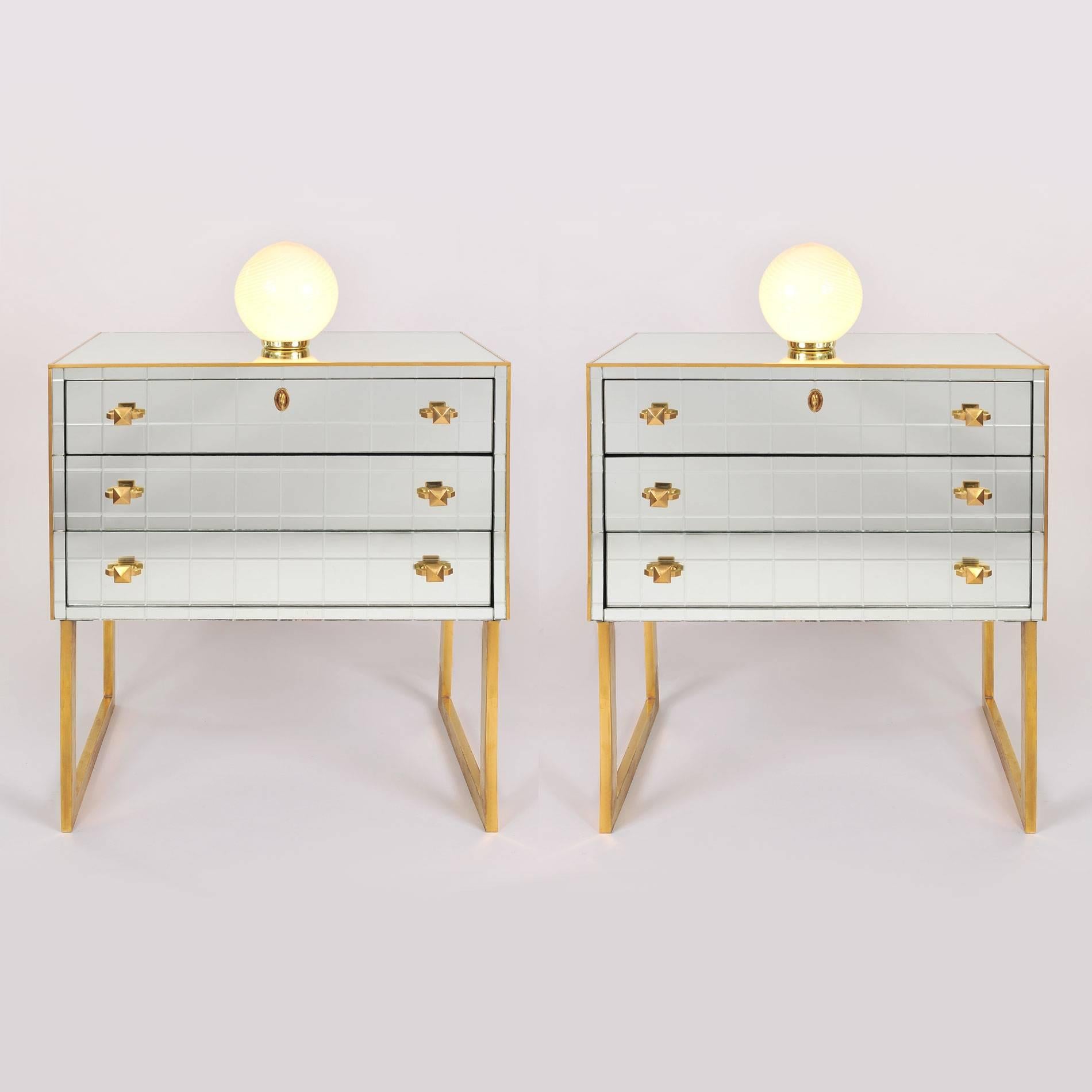 Pair of mirrored chests each with two drawers detailed with geometric brass and additional brass trim throughout, sitting on sculpted brass legs.