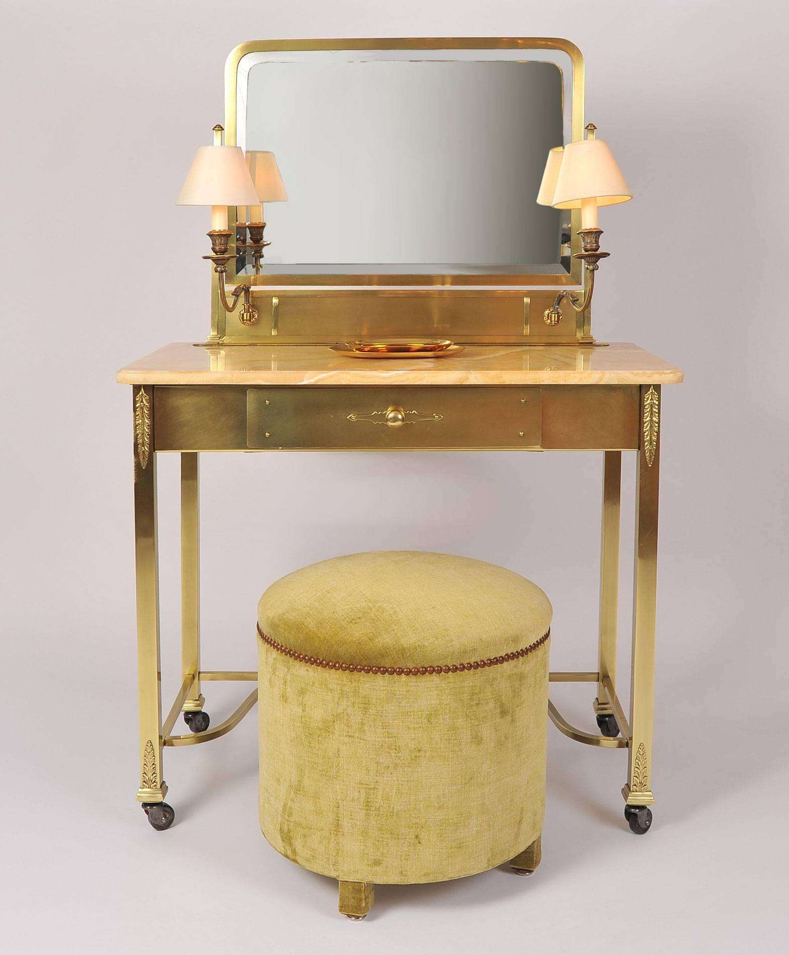 Well-proportioned brass dressing table or vanity with honey-colored marble top, on wheels, with single drawer, integrated rectangular mirror and lamp holders.