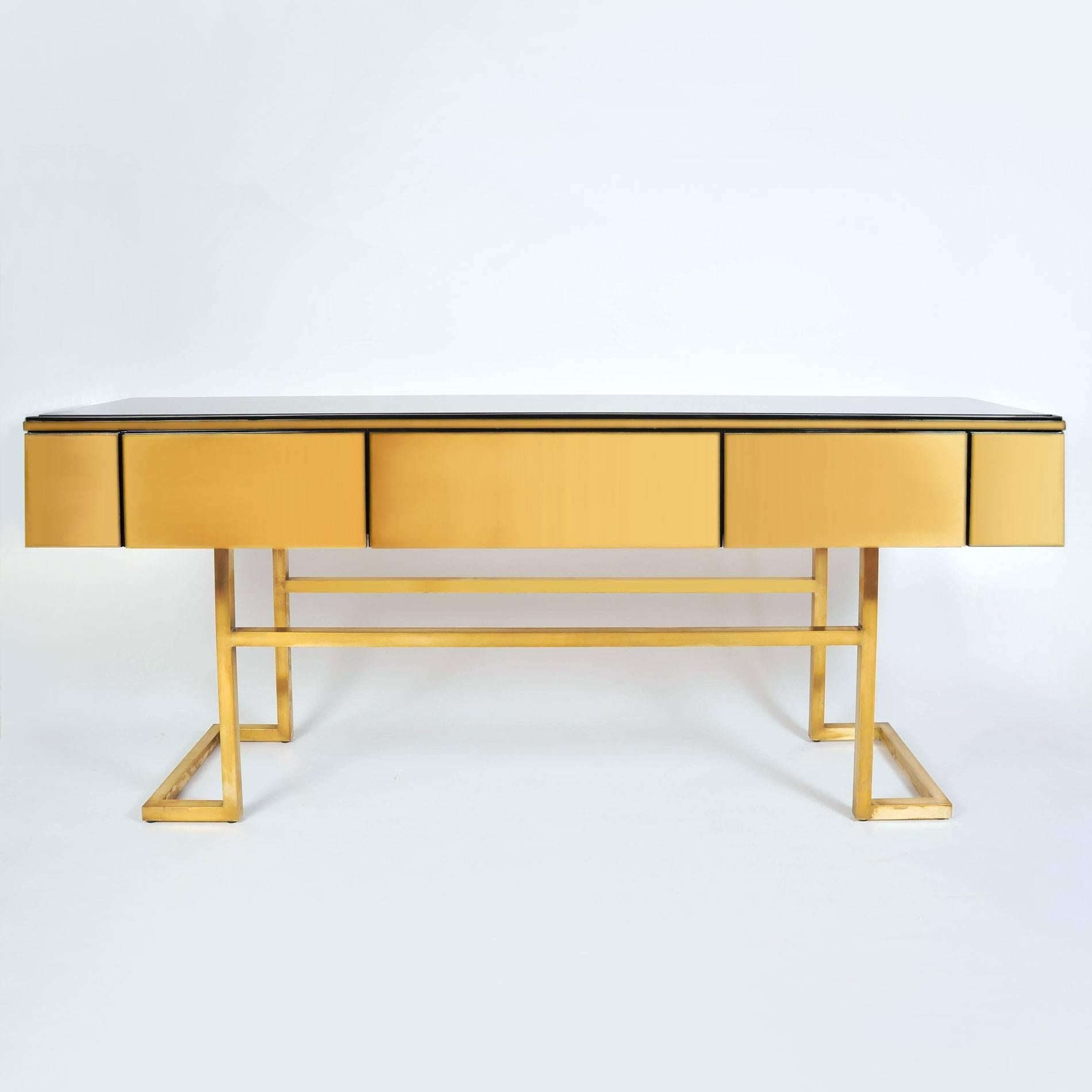 Super chic extra long sideboard with three rich brass drawers and side panels all supported on sleek brass legs. The contrasting top is glossy black lacquer under a protective glass top.