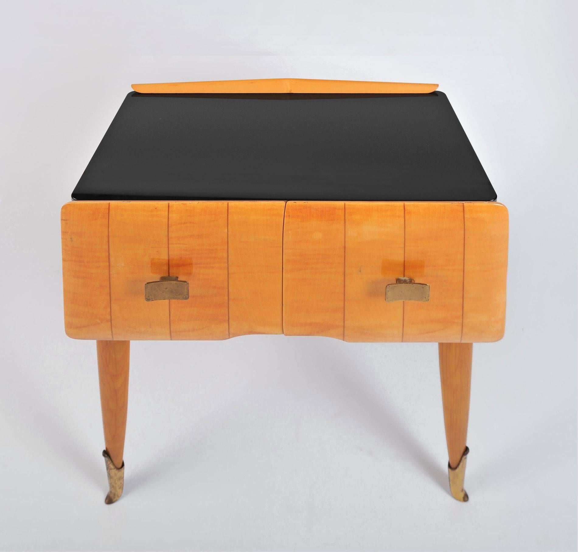 Pair of honey-toned birchwood nightstands with black glass tops. Each cabinet has eight wide matching stripes with doors that open left and right for storage. Further subtle detail of slim birchwood shaped back panel and original brass handles and