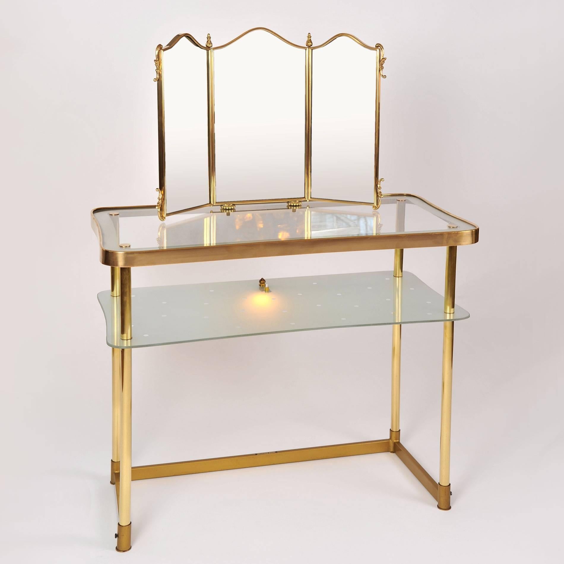 Two-tiered 1950s, vanity in brass with integral triptych mirror. The lower shelf is in etched glass with a polka dot design. A switch operates a fitted light, all on a rectangular base.