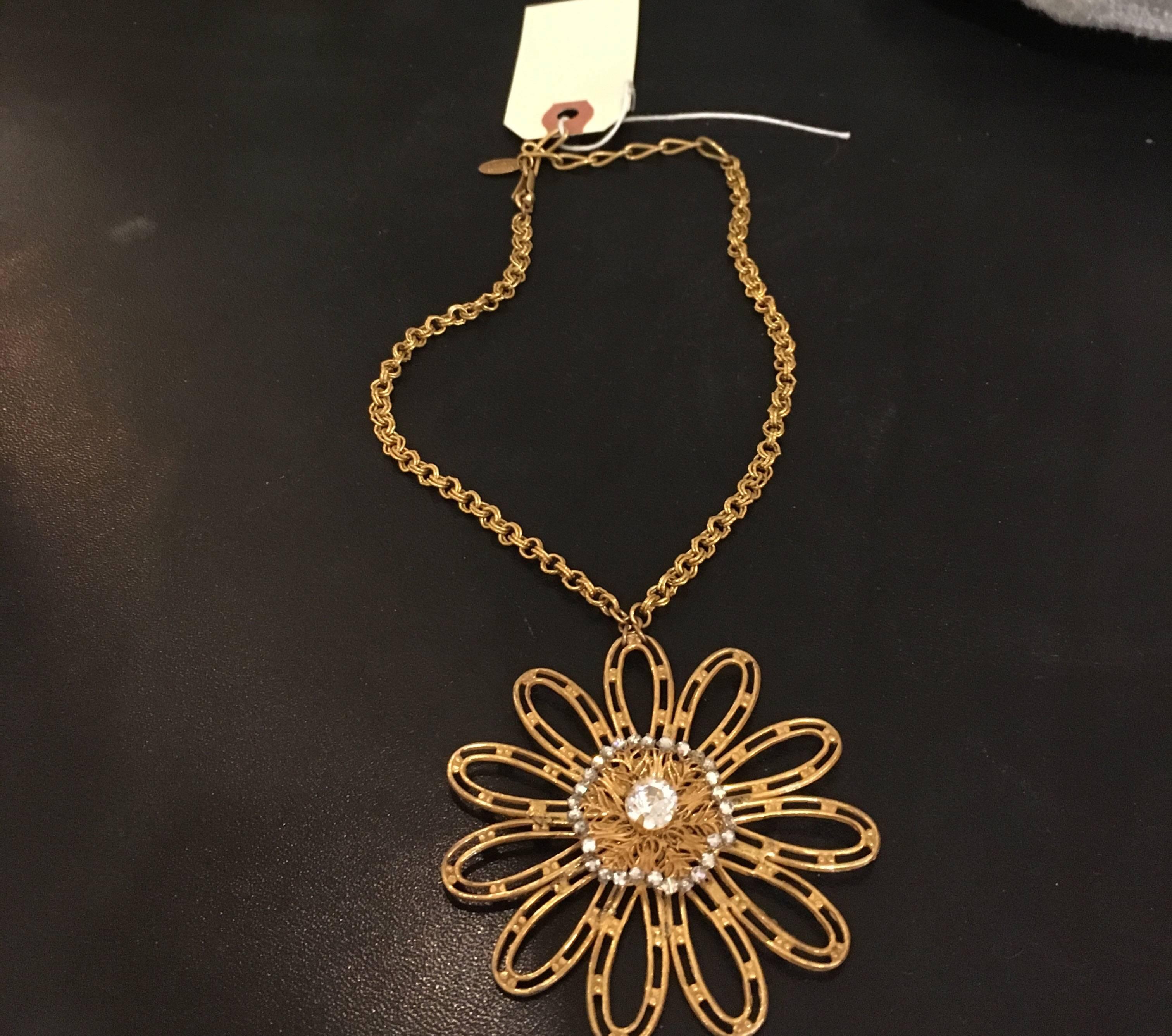 Large gold tone flower with filigree center ringed in clear stones on a gold.