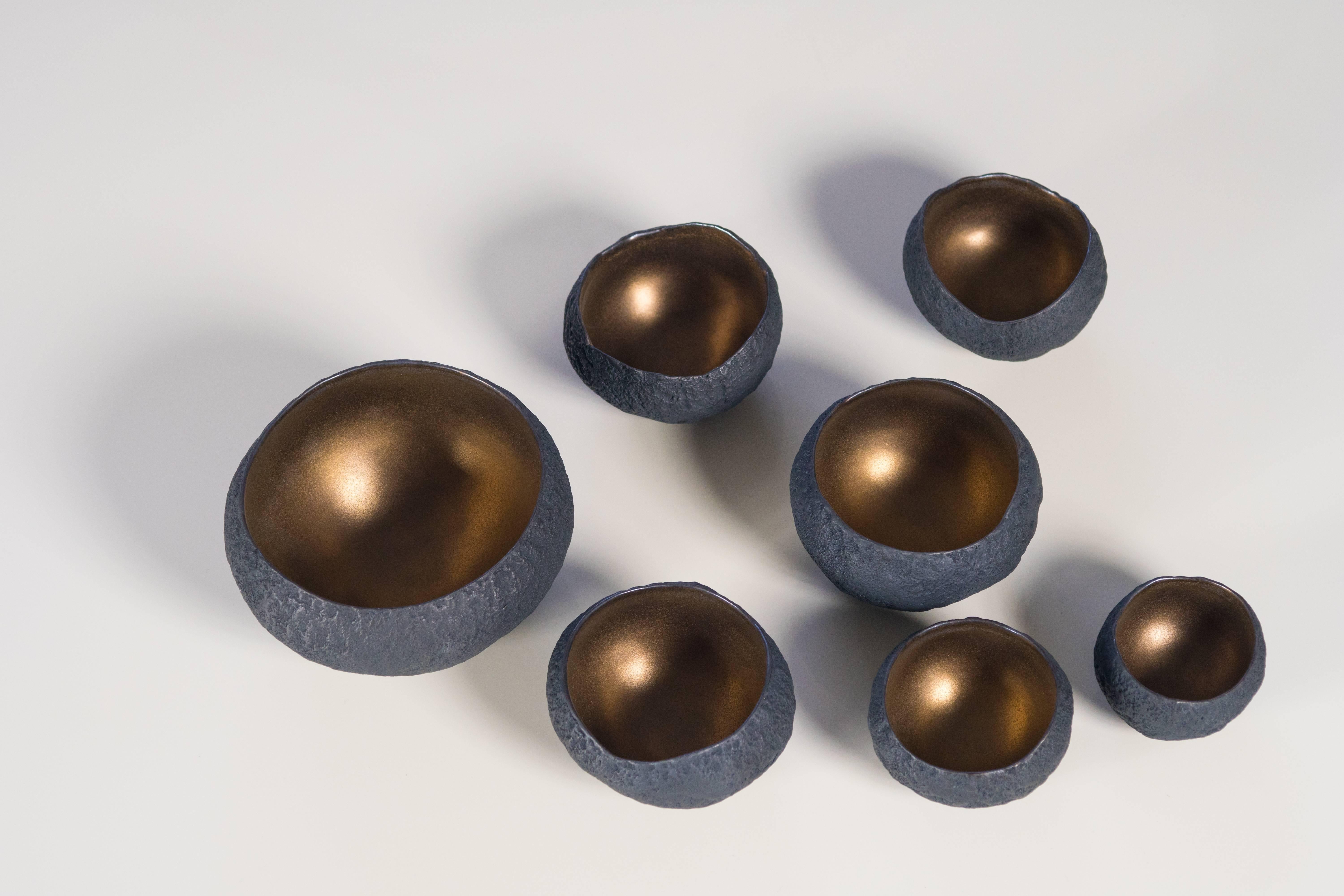 12 small and medium size bowls with bronze glaze interiors that can be purchased individually or as a 

Beginning with a ball of clay, she pinches it into vessels and textures them with stone fragments. After multiple firing it was glazed and
