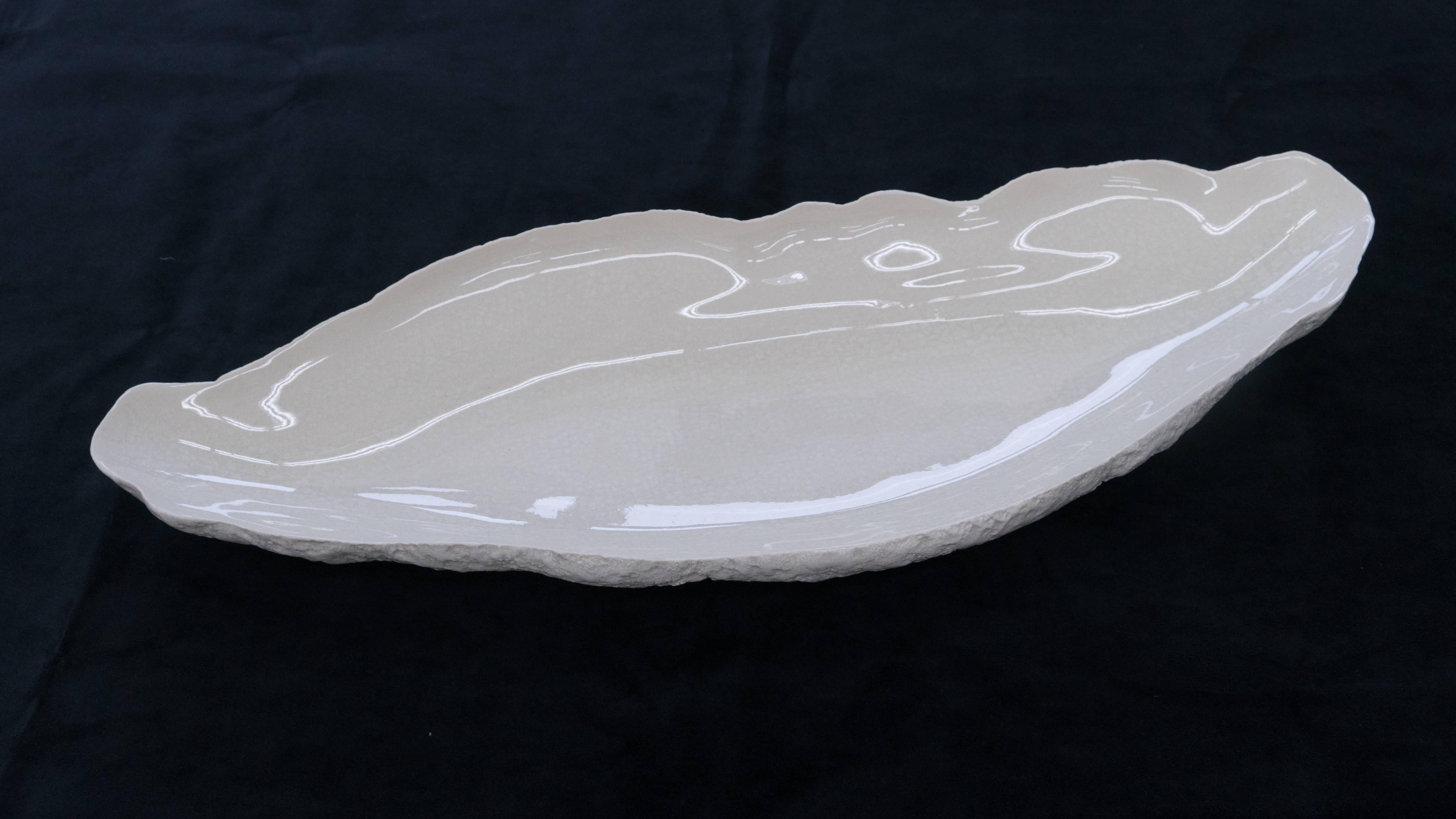 Large tray or platter in white ceramic. 

Beginning with a ball of clay, she pinches it into vessels and textures them with stone fragments. After multiple firing it was glazed and lustered. Its volcanic-like rough outer surface contrasts with the