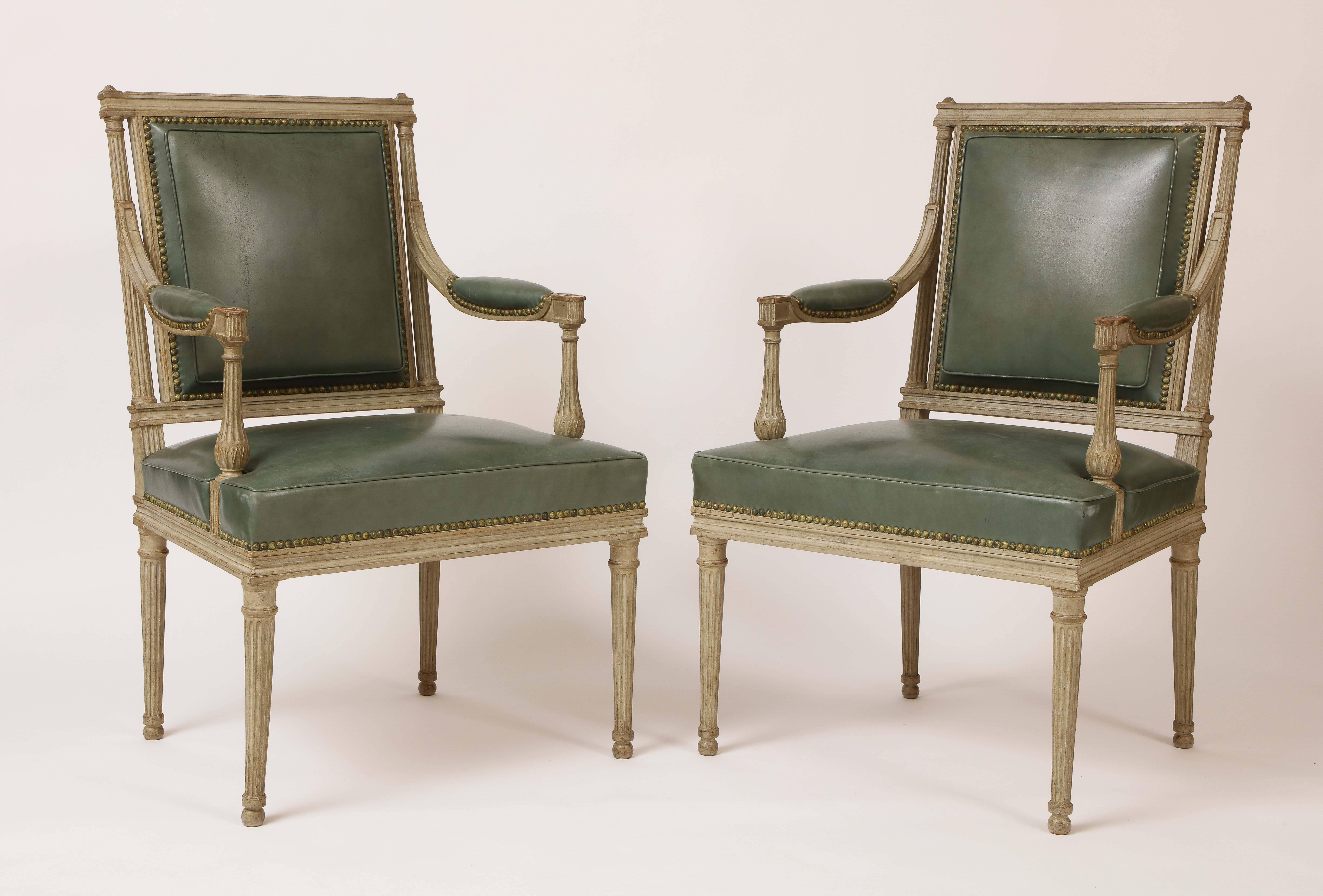 This fine pair of French neoclassical armchairs (fauteuils) was made by Maison Jansen. Made of grayish white painted beechwood with green leather upholstery, these chairs are in the Louis XVI taste with finely carved fluted columnar back supports