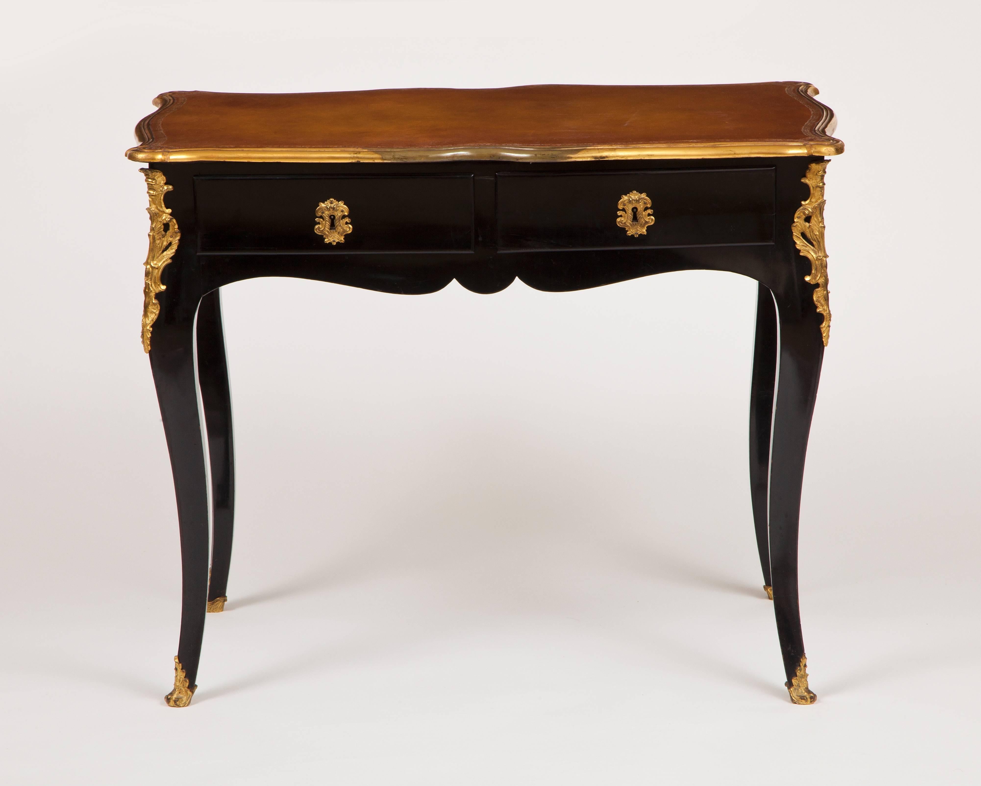 This fine French Louis XV period small writing table has a shaped top, with inset caramel colored tooled leather writing surface, banded with gilded bronze molding, above an ebonized wood frame with two drawers and an undulated apron, raised on