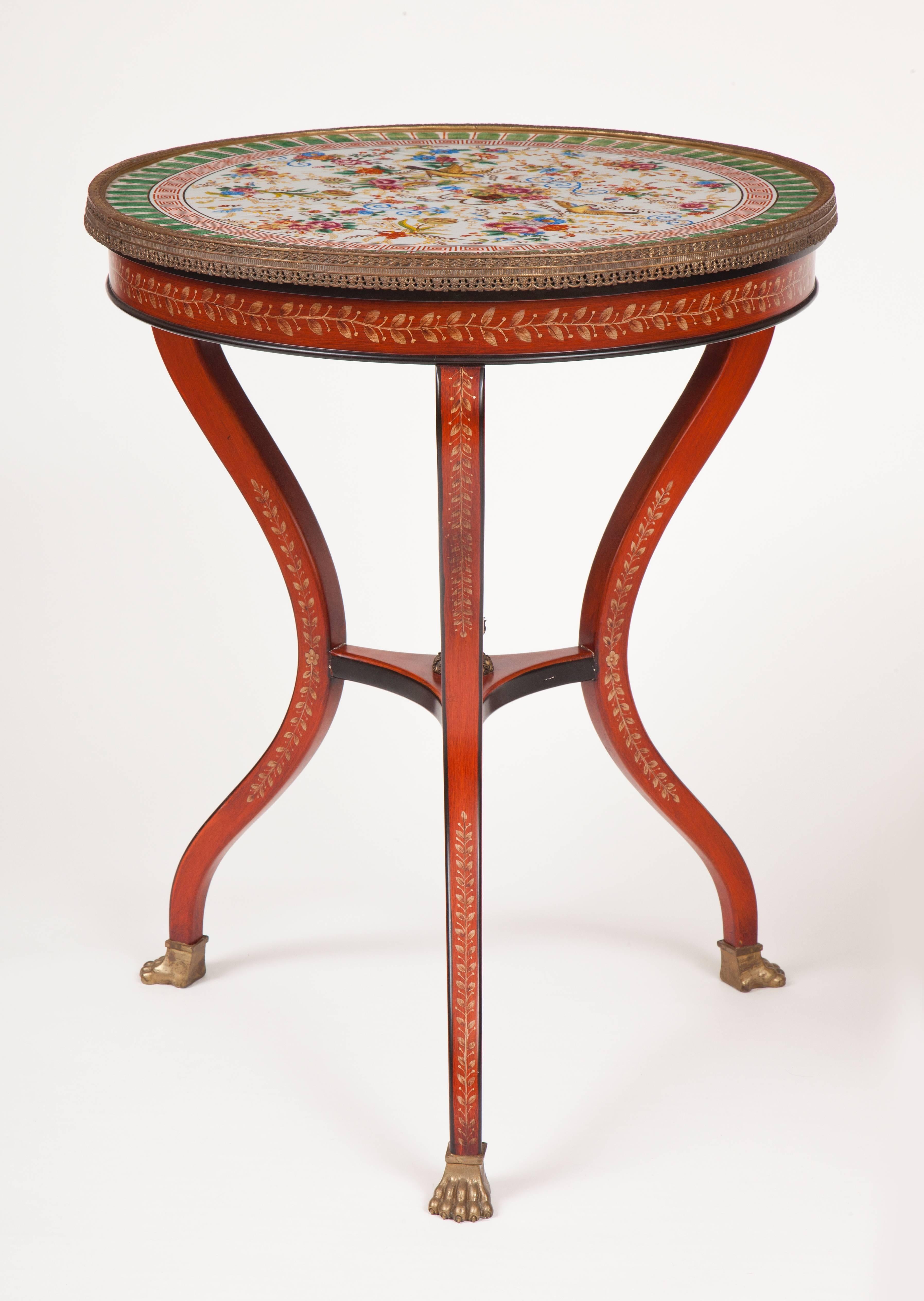 This pair of French tripod tables, or gueridons, each has a circular porcelain top in the Chinese family rose palette surrounded by a figured gilded bronze band above a red lacquered apron raised on three curved red lacquered legs joined by a