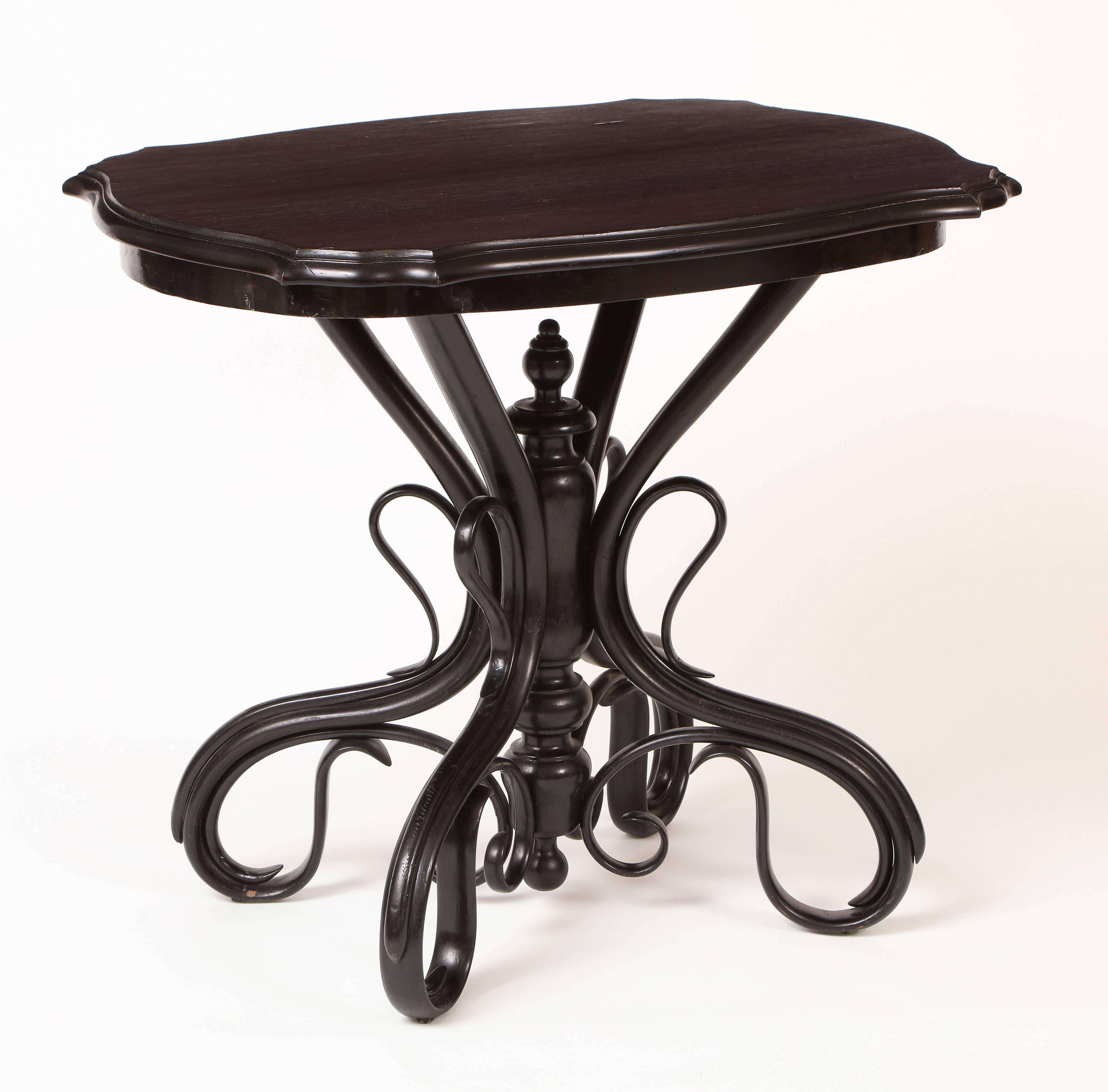 This bentwood table, with its shaped stained wooden top with molded edge and narrow apron resting on an ebonized base with central turned standard around which multiple intersecting curved bentwood elements are attached, was made in the late