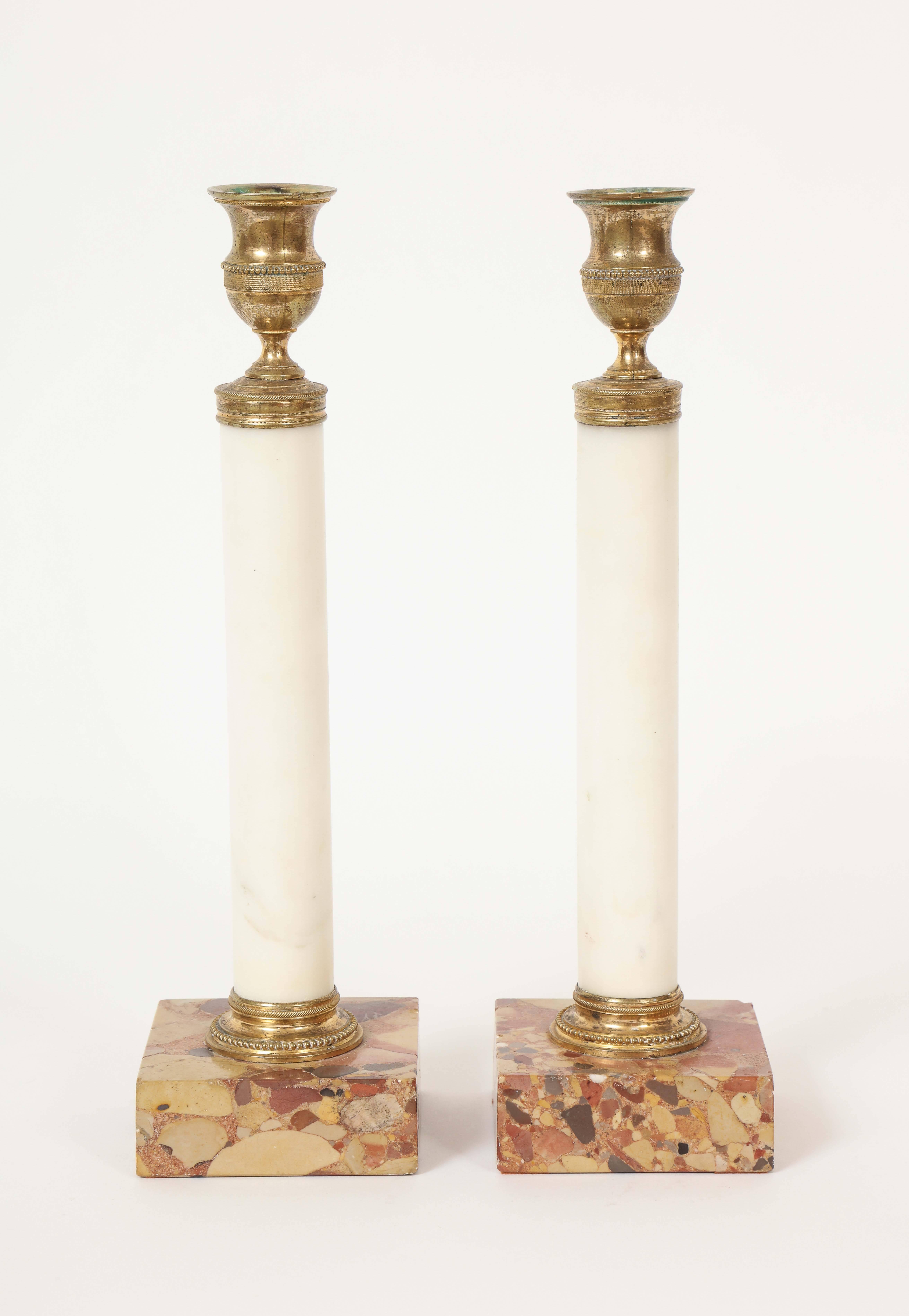 This pair of Swedish Gustav III period neoclassical candlesticks is each columnar in form, with a gilded bronze urn form candle bobeches, raised on a white marble column, with gilded bronze molded base, supported by a square mottled marble (breche