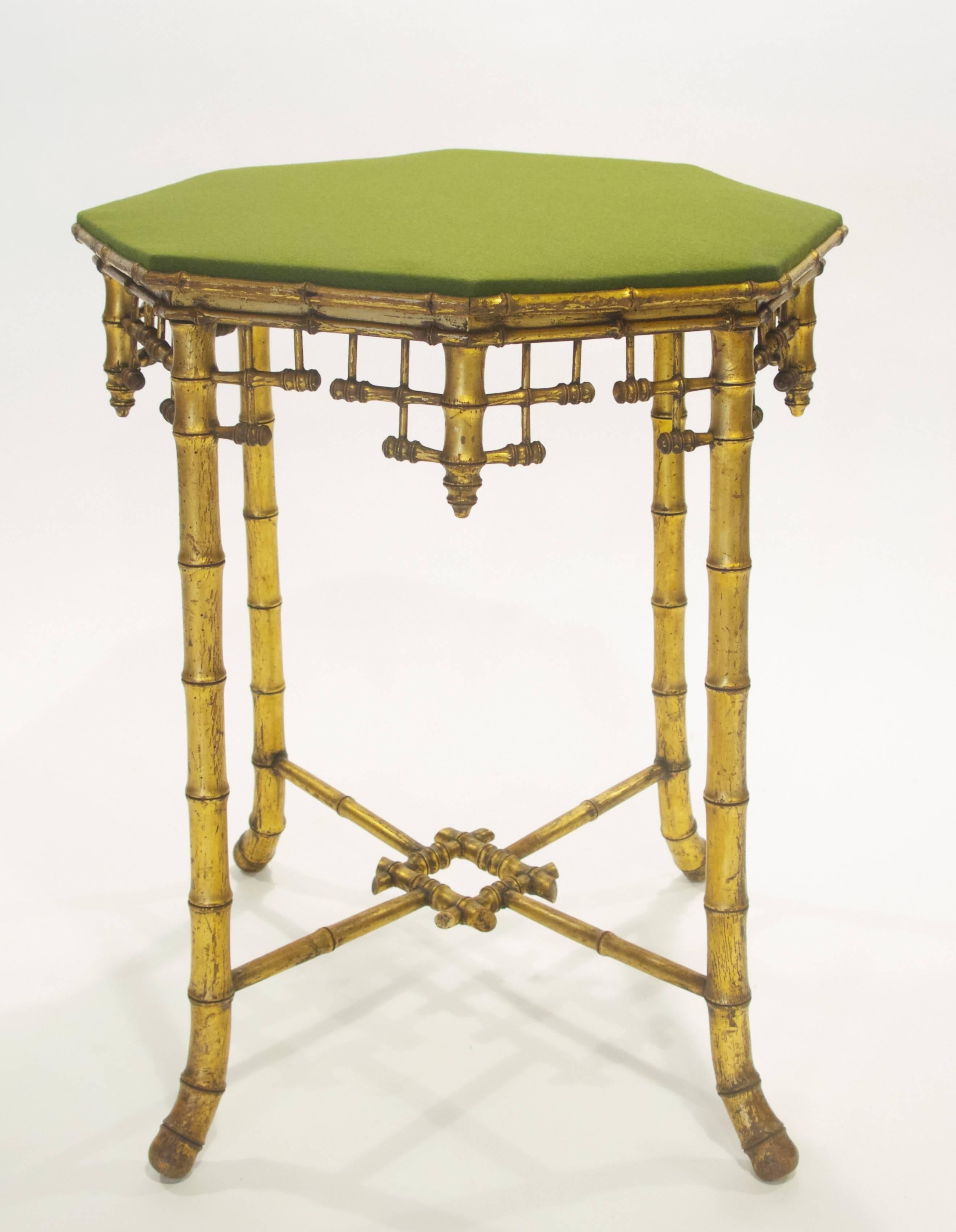 This French Napoleon III gilded wooden table has an octagonal top, covered in green wool felt, above faux bamboo fret work apron, raised on four faux bamboo legs, splaying out at the feet, joined by fax bamboo stretchers, centred on a faux bamboo