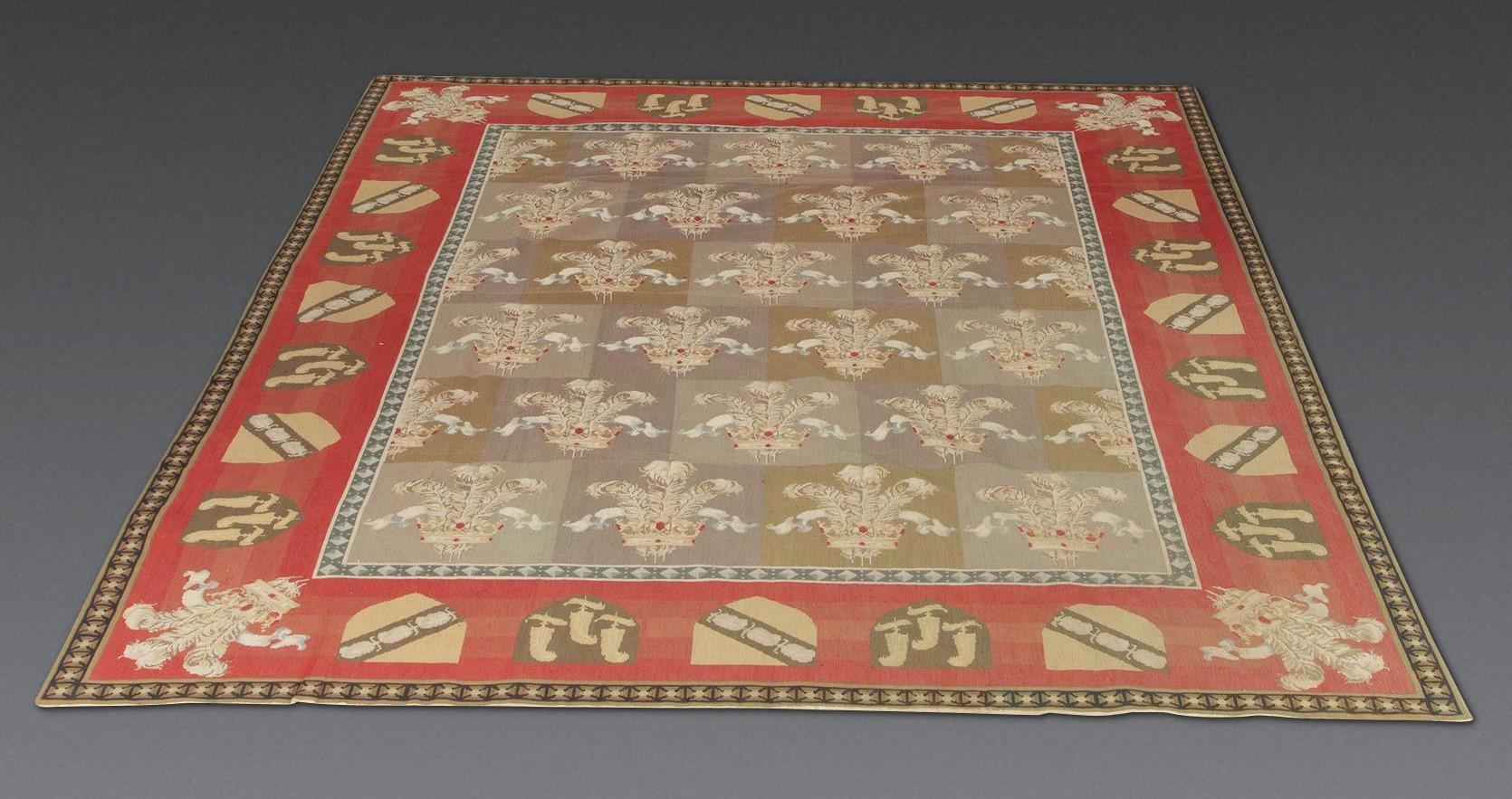 Grande tappeto decorativo ad ago inglese della fine del XIX secolo.
Il centro a scacchiera con piume del Principe di Galles. All'interno un bordo rosso di scudi araldici e ulteriori pennacchi di piume agli angoli. 
In buone condizioni, circa 1870. 