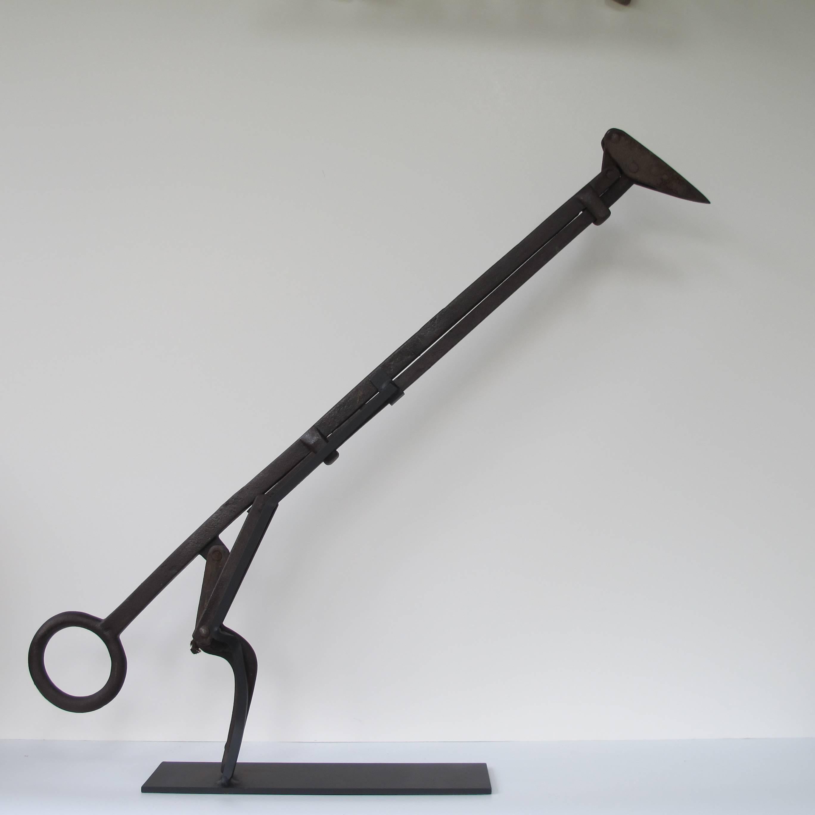 Mechanical iron tool for retrieving bales of hay. The nose spike goes into the hay bale and tilts from the handle to pull the bale of hay.
Mounted on an American Primitive black metal base at a raking 'bird-like' angle.