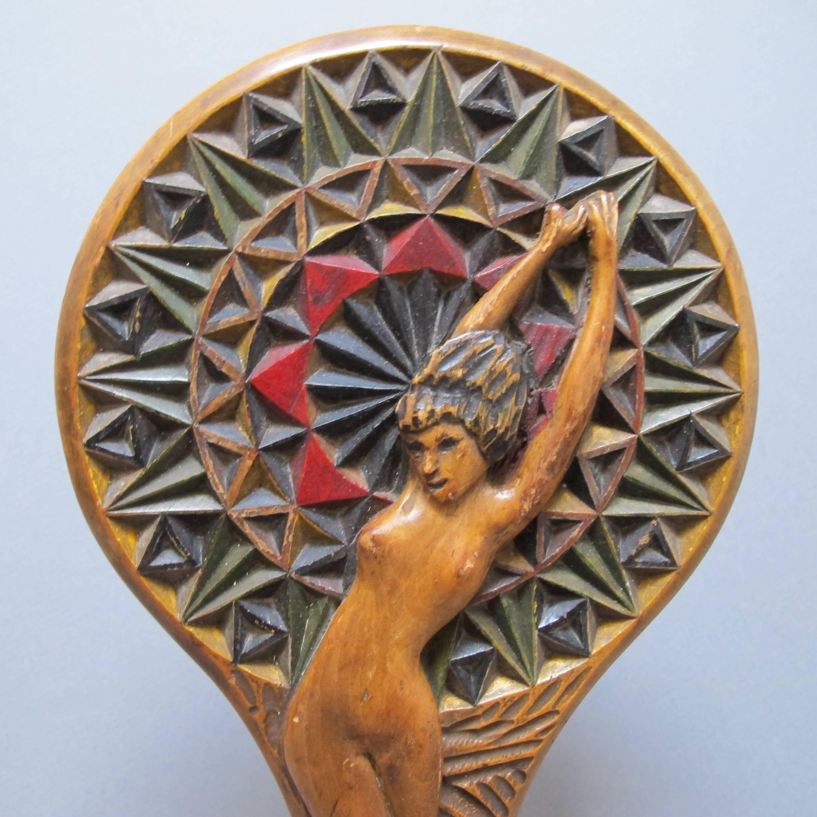 Carved and painted hand mirror with voluptuous nude at against a prismatic chip carved radiating pattern, The patterned colored handle suggests a Deco period with incised initials RS. Round beveled mirror glass. Mounted over a stepped metal base