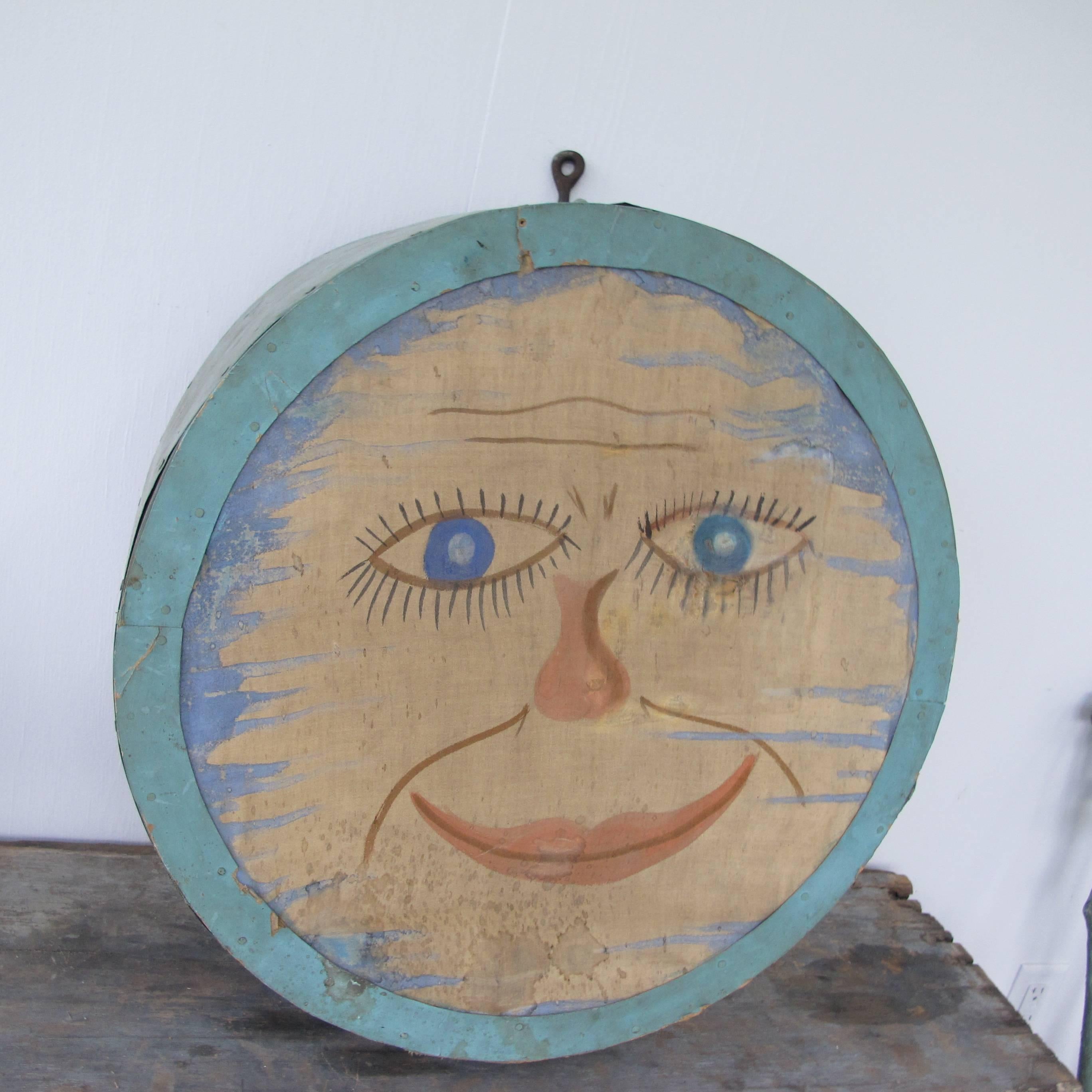 Unusual round painted fabric with smiling moon face stretched over a drum shaped wood form. The piece has a wood back with a hinged door that gives access to the two vintage light fixtures inside. The face is riveting with wisps of painted clouds