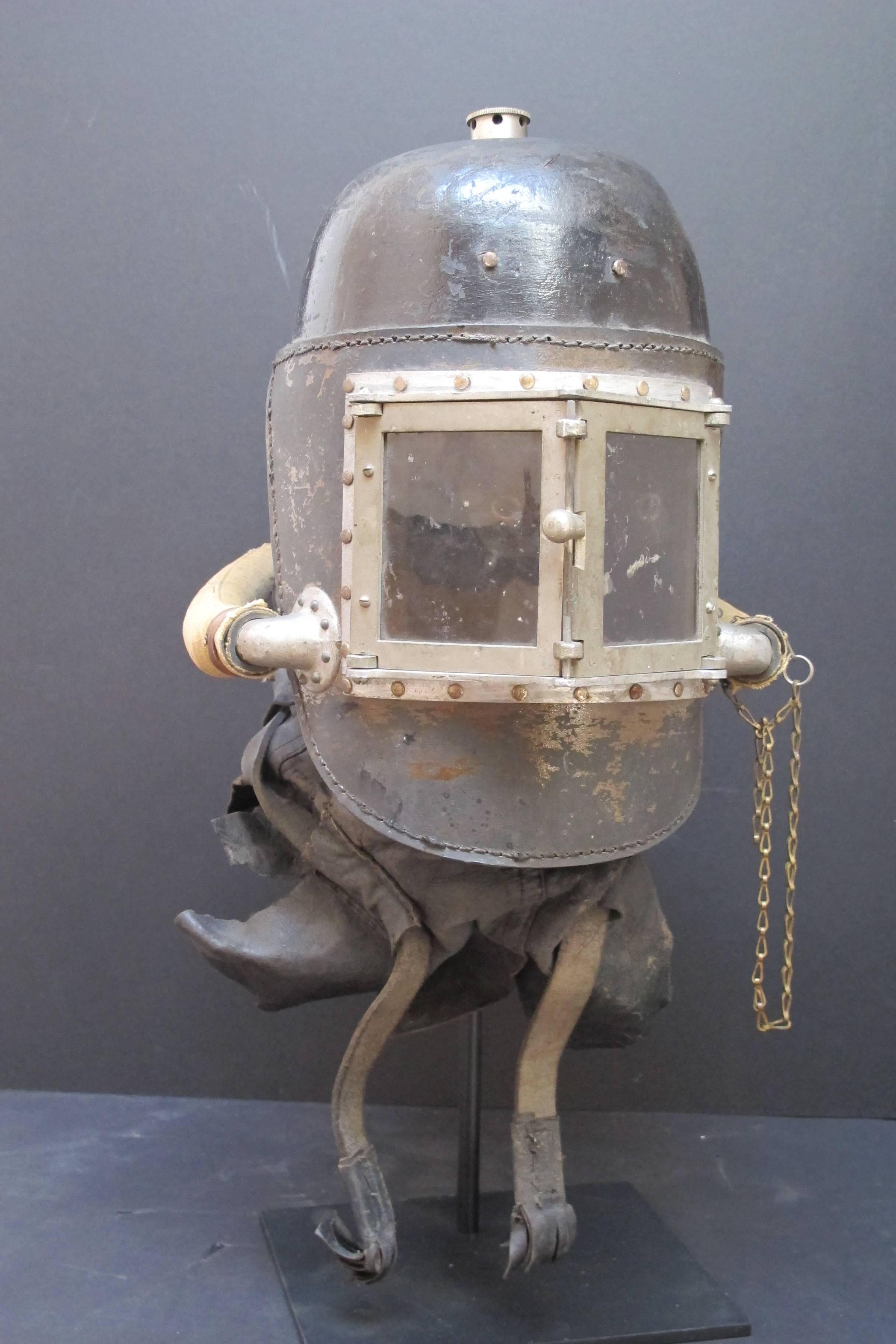 Unusual smoke helmet with a pair of hinged eye windows with mica to protect the eyes and open for needed viewing. The helmet retains the double hoses coming to the back which supplied fresh air from someone on the outside that operated a foot pedal