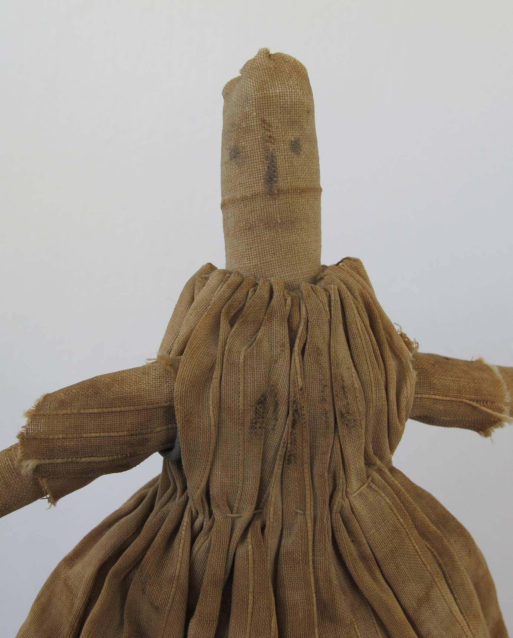 Simple cloth doll of homespun linen with rolled arms and legs and head. The gathered dress was once blue and is now a mottled tan. Pictured in American Folk Dolls by Wendy Lavitt - full page. Mounted on American Primitive metal base.