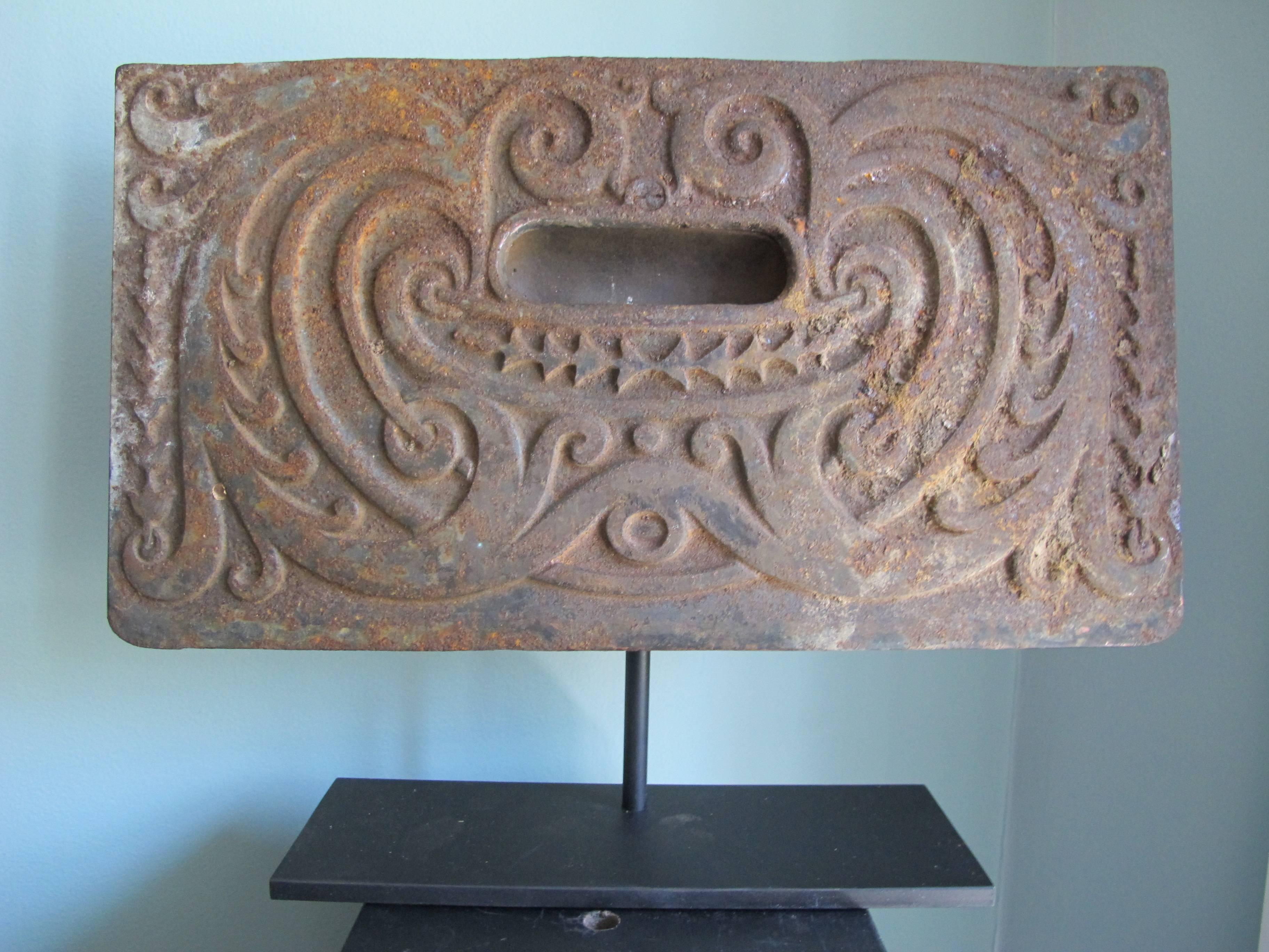 Graphic stove vent door with elaborate scroll work designs in relief. Making a face. Mounted over metal base.