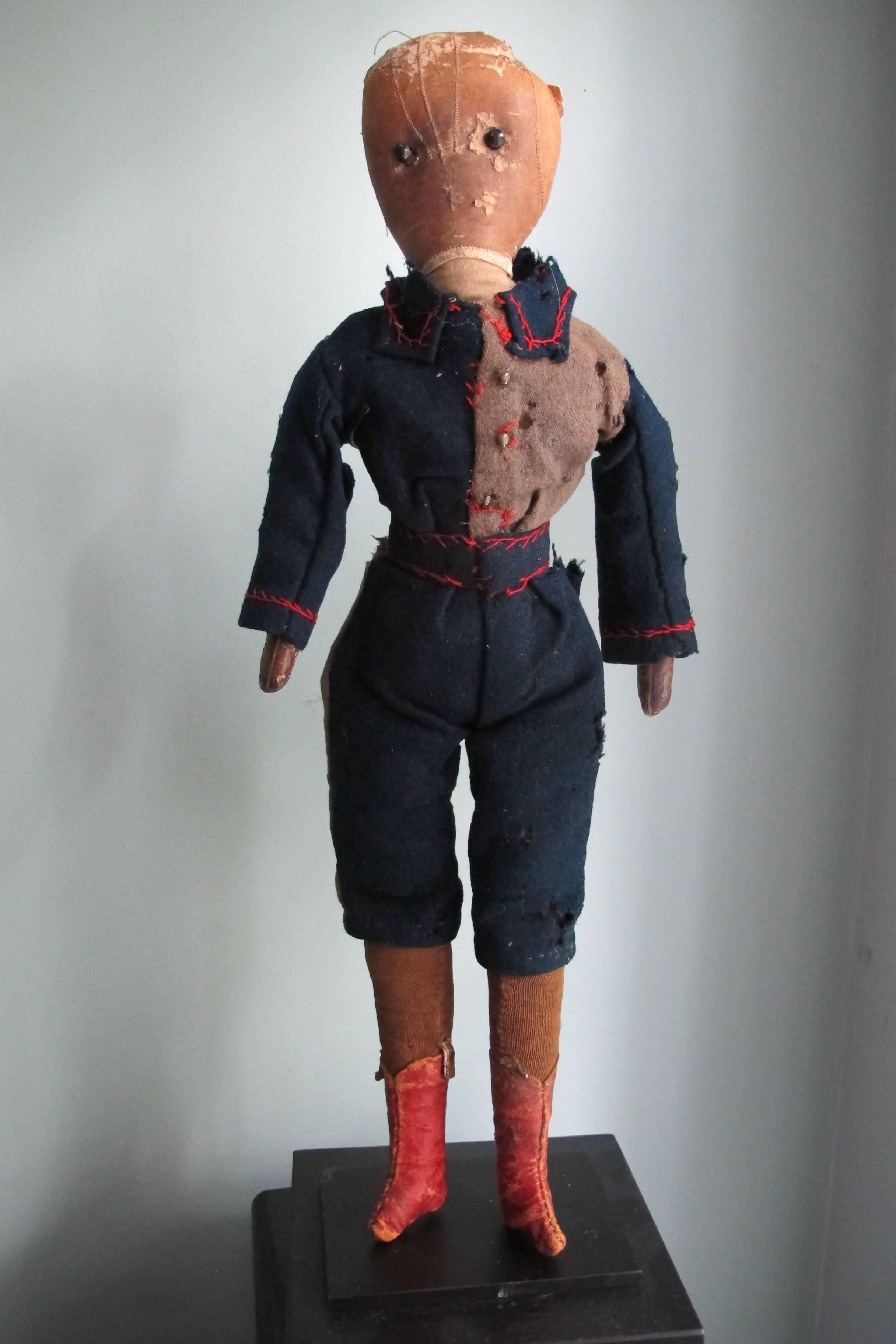 An early boys doll with fancy pants and jacket with head made for a stitched leather child's glove and red leather boots. The eyes are applied black shoe buttons. The doll came with a yellowed paper note , 