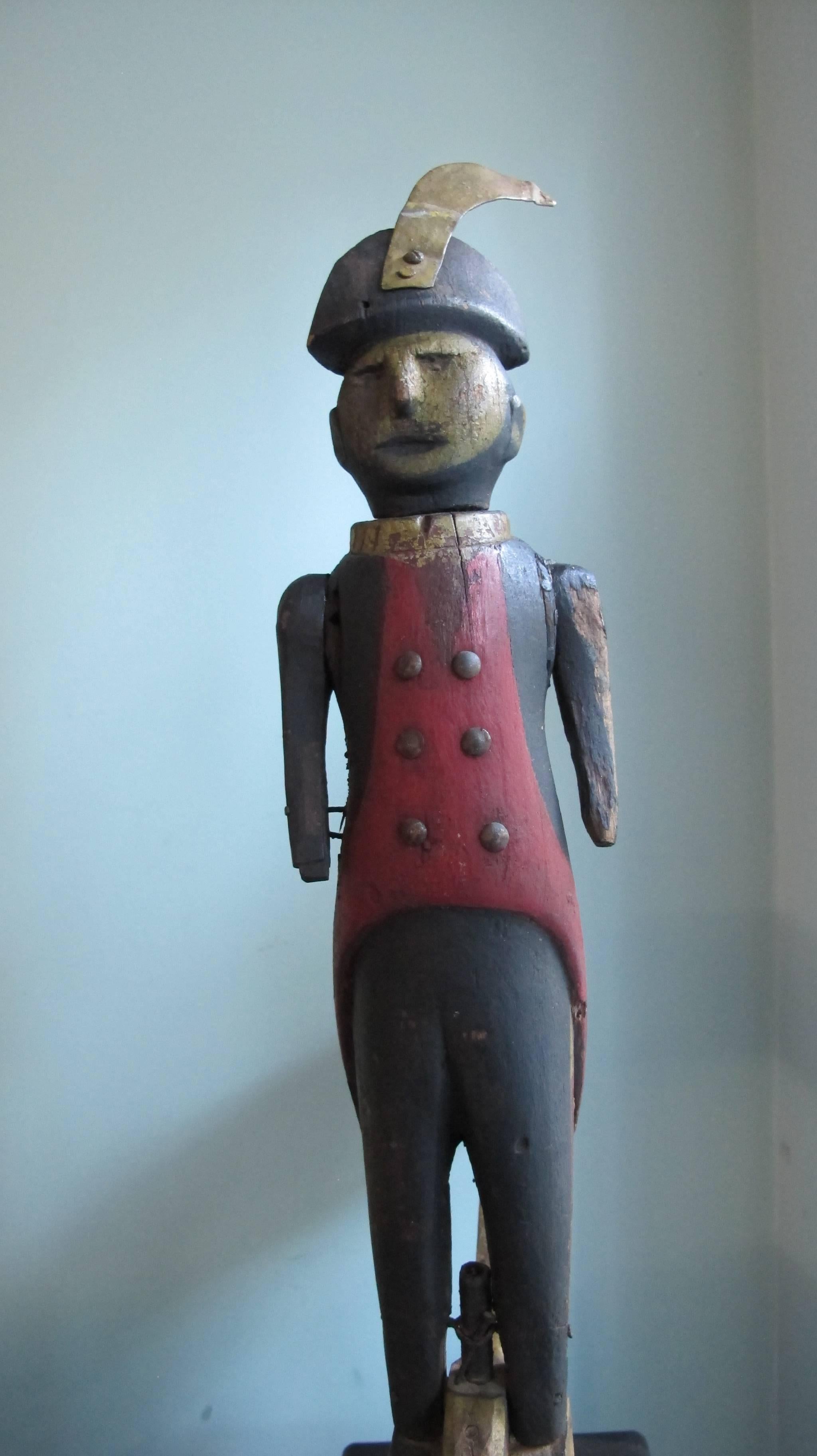 Carved and painted soldier standing on arrow whirligig that also worked as a weathervane with the wooden arrow pointing the wind direction. The figure is wearing a revolutionary war uniform with metal tack buttons and long red tails with stripes on