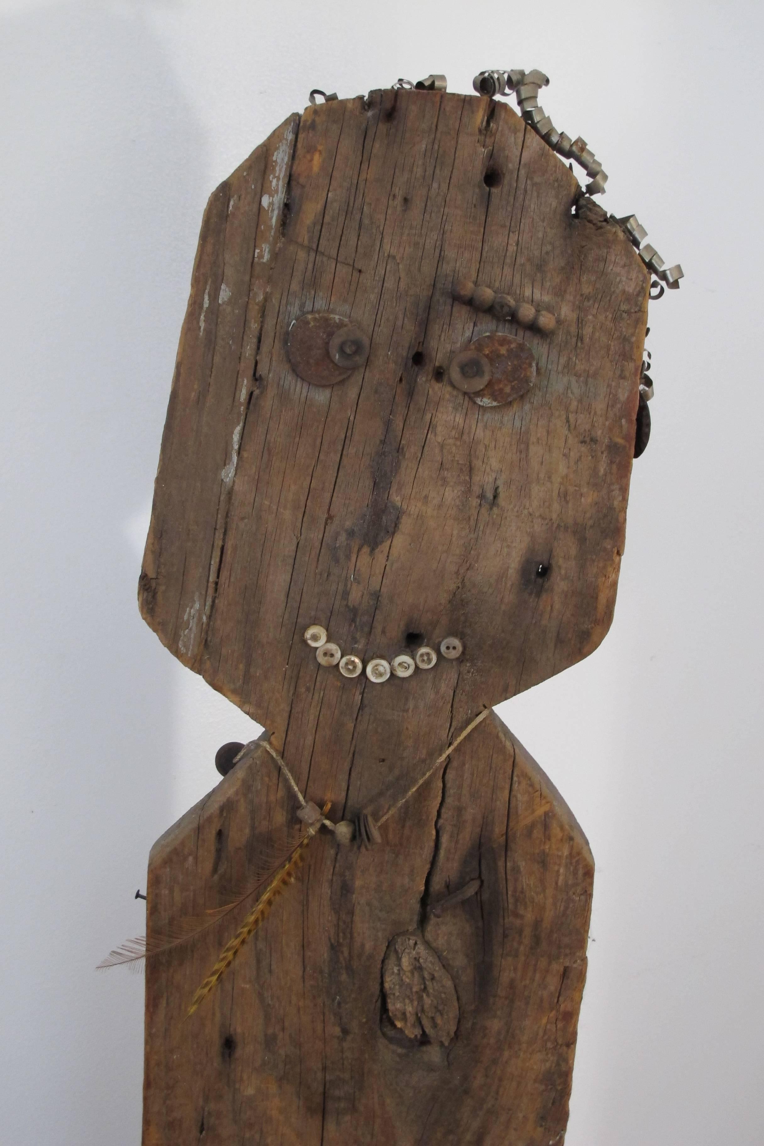 Wood yard show figure originally found in Maine. The unpainted 
figure has applied metal for eyes with buttons for eyes and curled metal for hair. There is a stringed necklace with beads and feathers. A cloth wrap serves as a loincloth. Mounted on