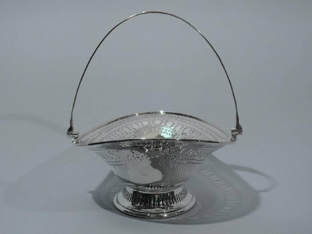 Edwardian sterling silver basket. Made by Walker & Hall in Sheffield in 1902. Ovoid with tapering sides and flared rim. Rests on raised ovoid foot. Tapering swing handle. Solid well bordered by pierced and engraved ornament. Foot has linear
