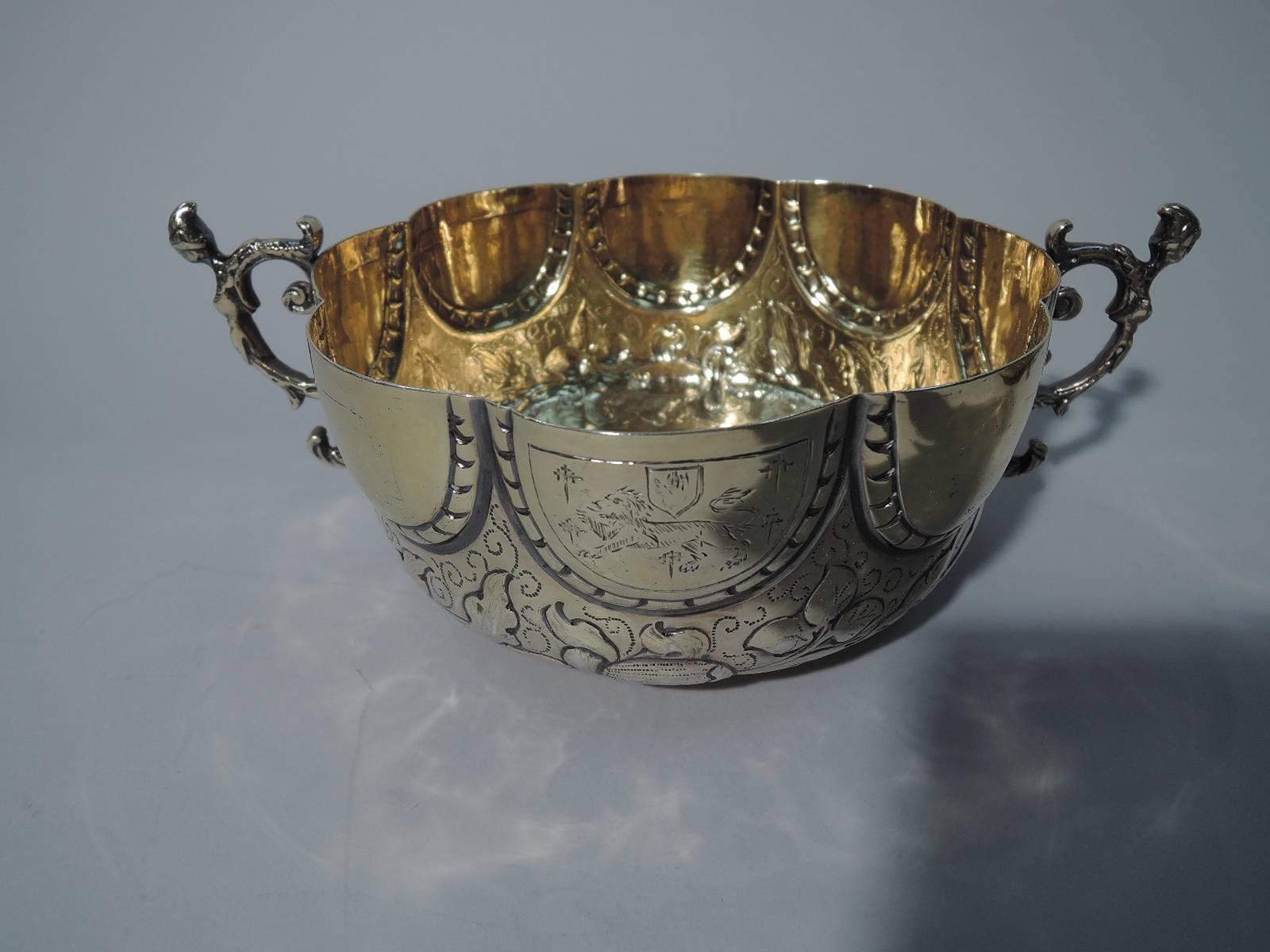 Pair of antique silver gilt bowls in late 17th-century English style. Each: round with short foot and leaf-capped double-scroll handles. Lunettes (one with engraved armorial), and flowers and foliage. Pretty pieces in Ye Olde English taste.