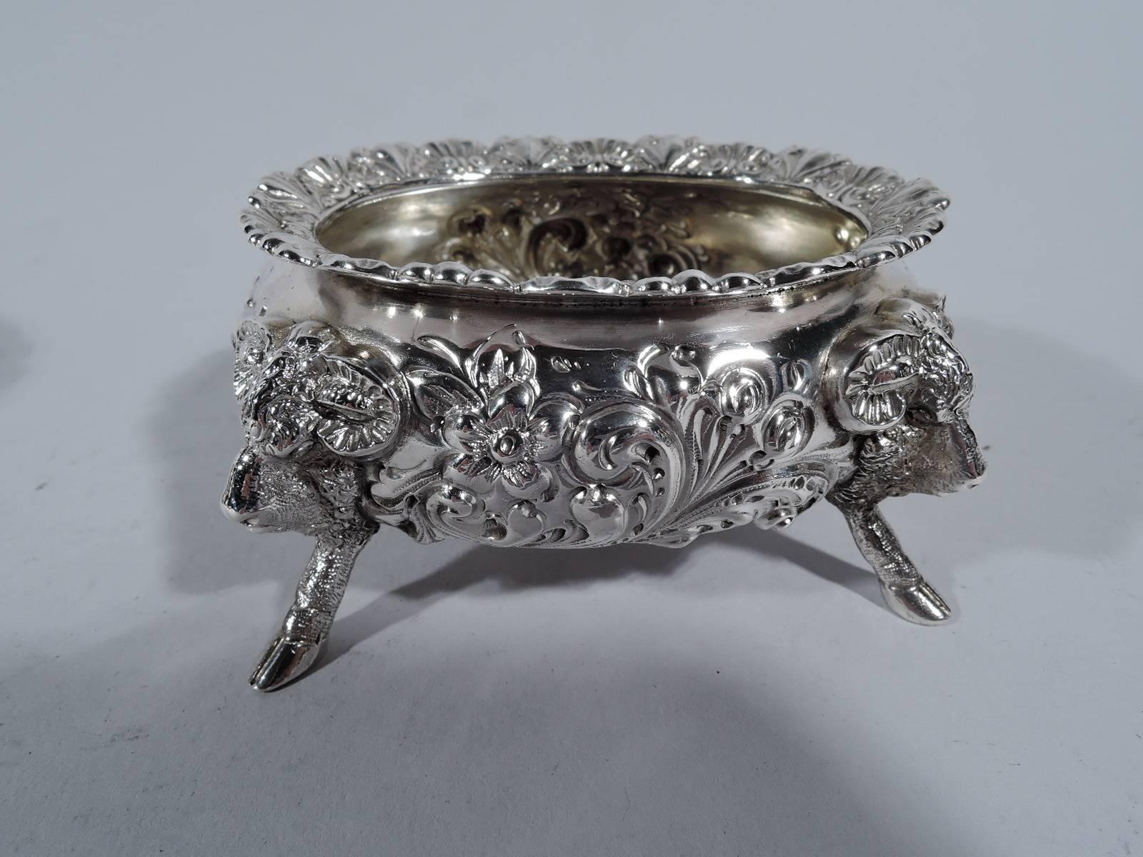 Pair of Neoclassical-style sterling silver open salts. Made by Howard in New York in 1897. Each: Bellied bowl with floral repousse and monopodia supports in form of ram’s head terminating in hoof. Interlaced script monogram engraved on underside.