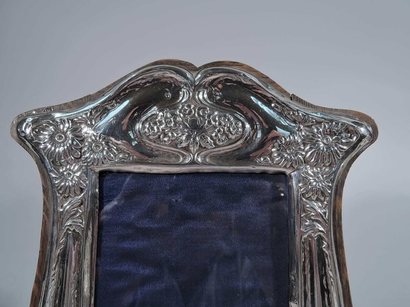 Art Nouveau sterling silver picture frame. Made by J. Aitkin & Son in Birmingham in 1909. Bombe sides, bracket feet, and shaped top. Symmetrical whiplash lines with flowers. Frame mounted to stained-wood with hinged support. Rectangular window with