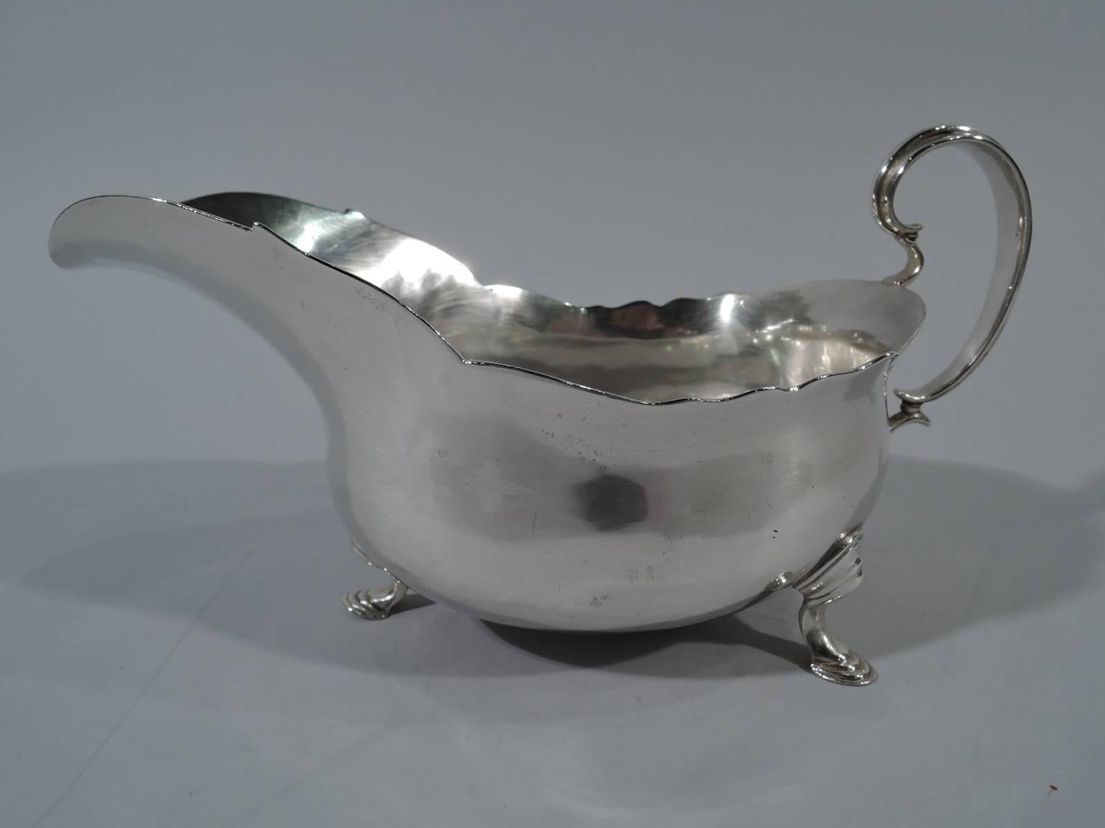 George III sterling silver gravy boat. Made by John Parker & Edward Wakelin in London in 1770. Curved bowl with helmet mouth and high-looping double-scroll handle. Rests on 3 hoof supports. Sturdy Georgian with nice heft. Hallmarked. Weight: 9.5