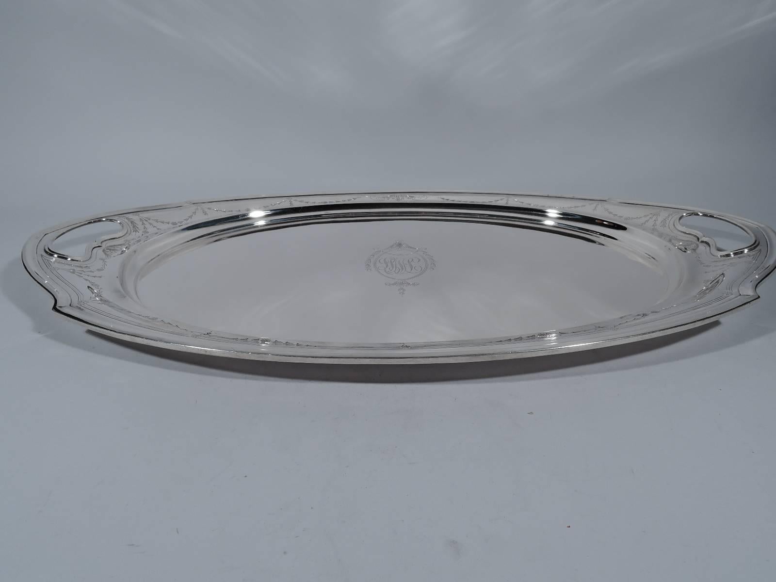 Edwardian sterling silver tea tray. Oval well with shaped and molded rim and pointed ends with cut-out kidney handles. Engraved Regency garland on shoulder. Well center has same style frame with interlaced script monogram. Hallmarked Joseph Seymour