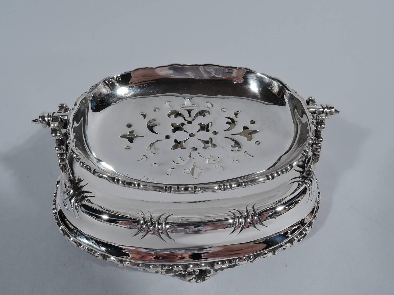 Victorian sterling silver soap dish. Oval stand with well and applied pierced and scrolled foot. Pierced scroll brackets support swing-mounted bowl with scrolled rim and pierced ornament. A practical and innovative design in the old-fashioned style.