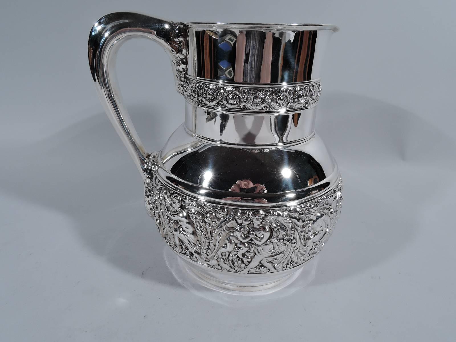 Sterling silver water pitcher in Olympian pattern. Made by Tiffany & Co. in New York. Globular with drum-form neck, small lip spout, and leaf-mounted handle. Rinceaux frieze inhabited by harp-strumming, love-making, and peekaboo-playing figures.