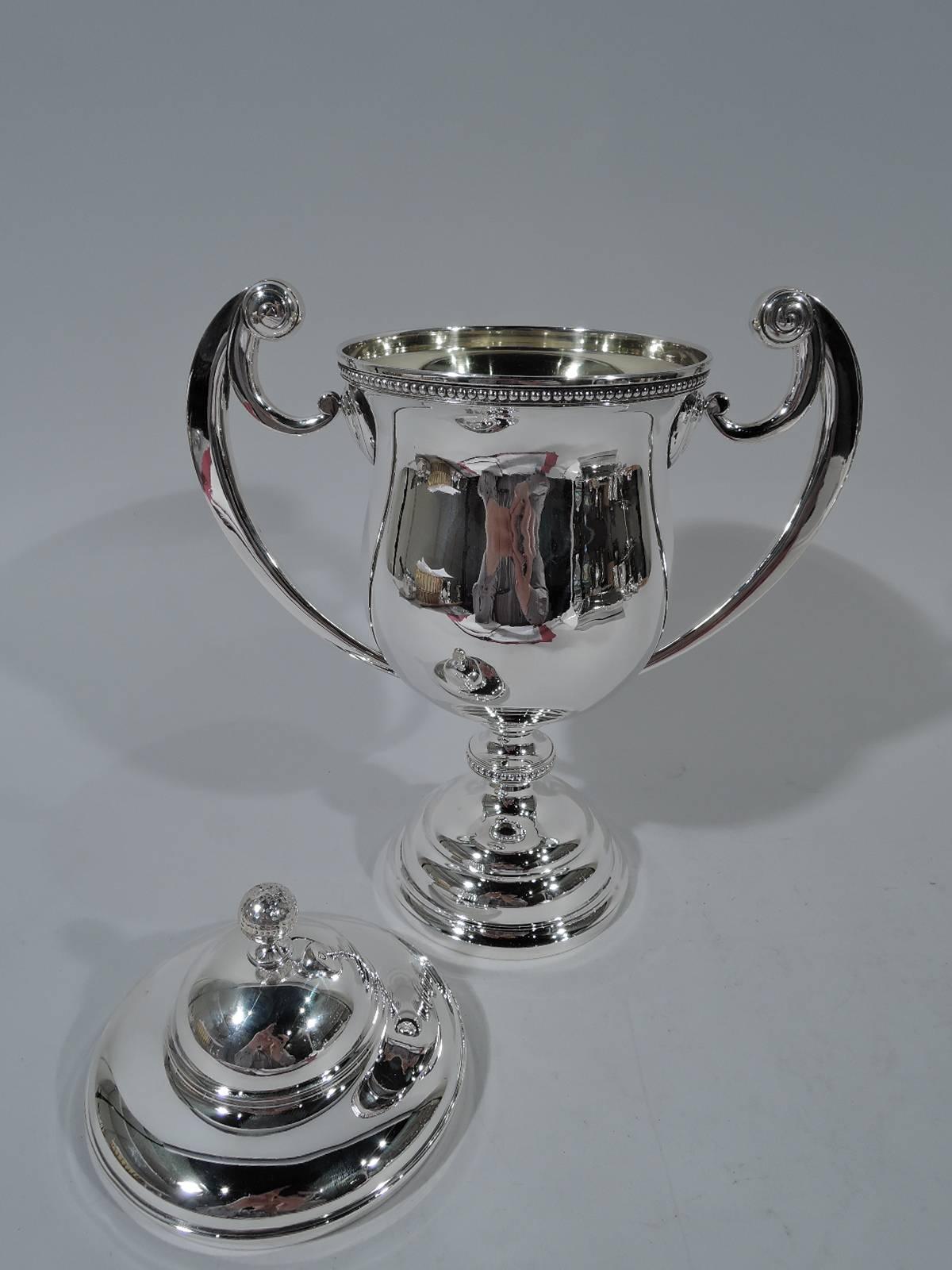 American sterling silver trophy cup, circa 1920. Urn body with beaded rim and knop, flying scroll side handles terminating in volutes, and double-domed foot. Cover also double-domed with golf ball finial. Cup and cover interior gilt. Lots of room