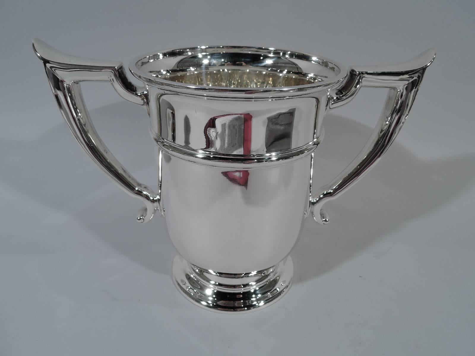 Classic sterling silver trophy cup. Made by Gorham in Providence in 1929. Straight sides with capped scroll bracket side handles and stepped round foot. Spare and elegant with one raised band. Hallmark includes no. A13712 and date symbol. Weight: 33