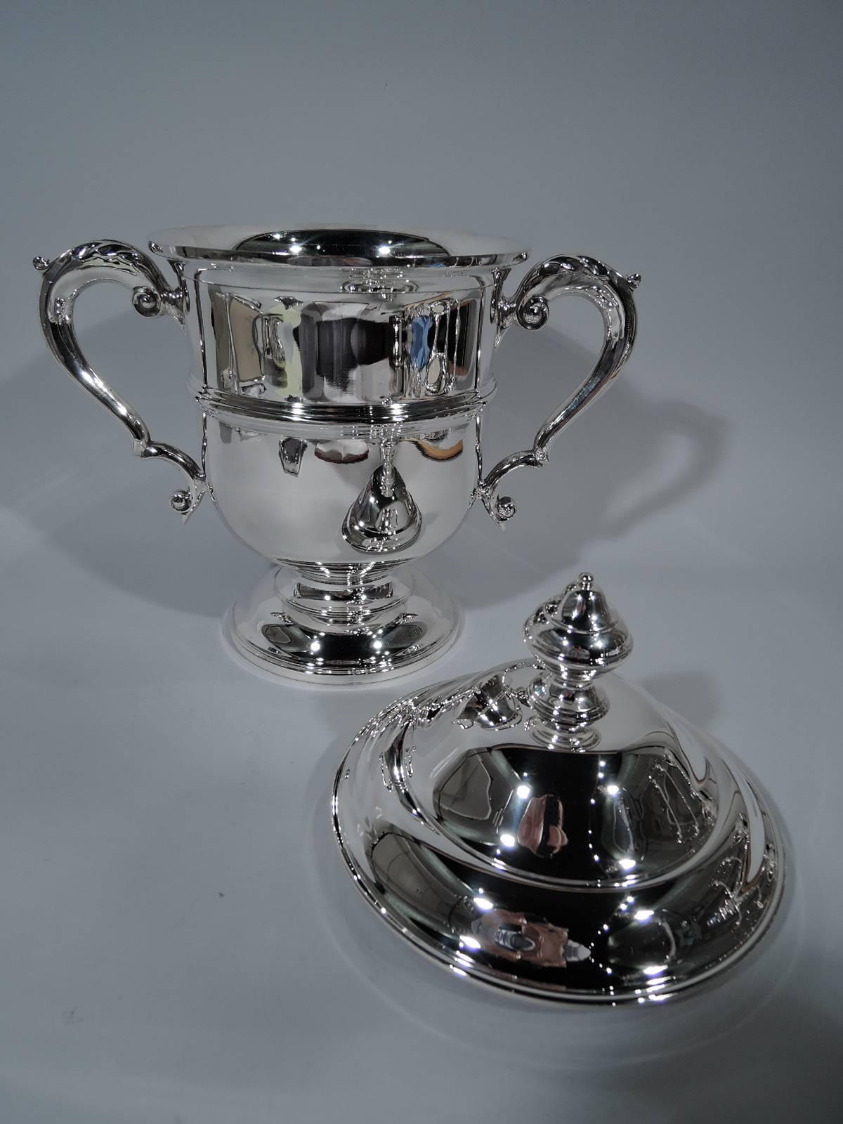 Traditional sterling silver covered trophy cup. Retailed by Tiffany & Co. in New York. Urn with leaf-capped double-scroll sides handles, raised foot and molded band. Double-domed cover with vase finial. A large version of the classic form with