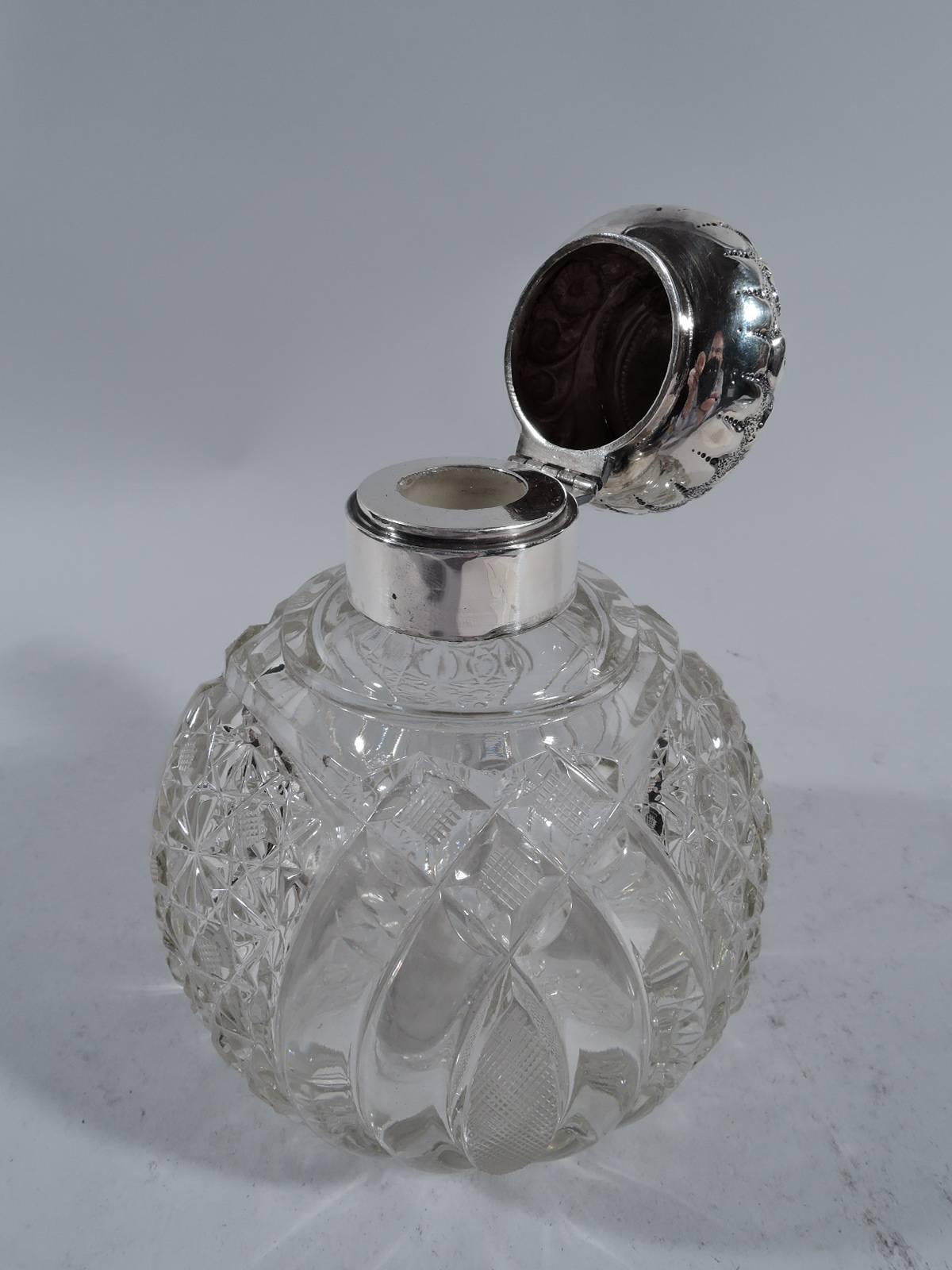 Edwardian clear glass perfume bottle with sterling silver mount. Made in Birmingham in 1901. Globular with diaper pattern and C-scrolls. Short neck has silver collar with hinged bun cover. Cover has repousse flowers on stippled ground and scrolled