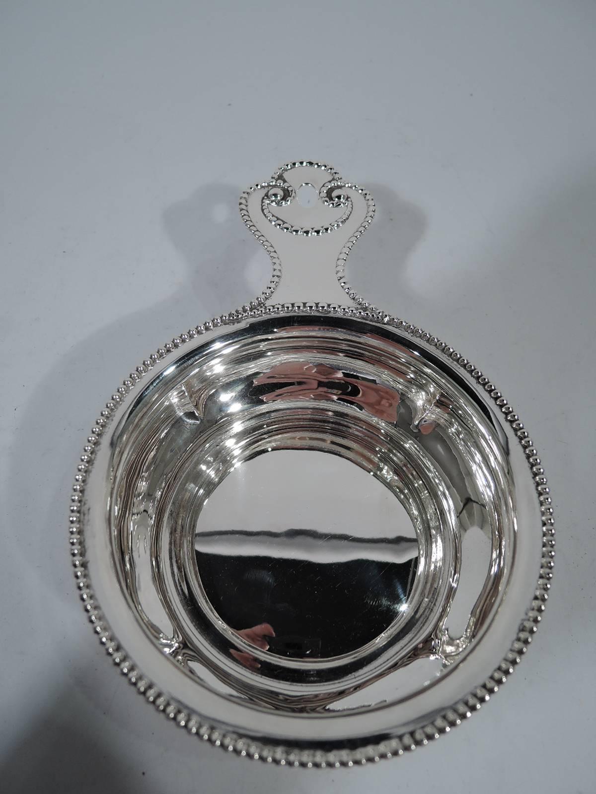 Sterling silver porringer. Made by Towle in Newburyport. Crimped bowl and solid handle with pierced oval. Beaded bowl and handle rims as well as beaded volute scrolls on handle. Jazzed-up tradition. Hallmark includes no. 105 and retailer’s name