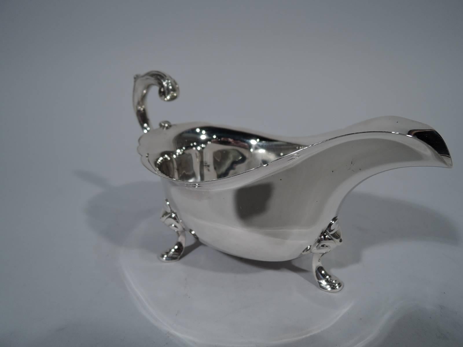 Wartime sterling silver gravy boat in Georgian style. Made by Tiffany & Co. in New York. Helmet mouth with scalloped rim and leaf-capped flying double-scroll handle. Rests on three hoofs with volute scroll mounts. A nice traditional piece made in a