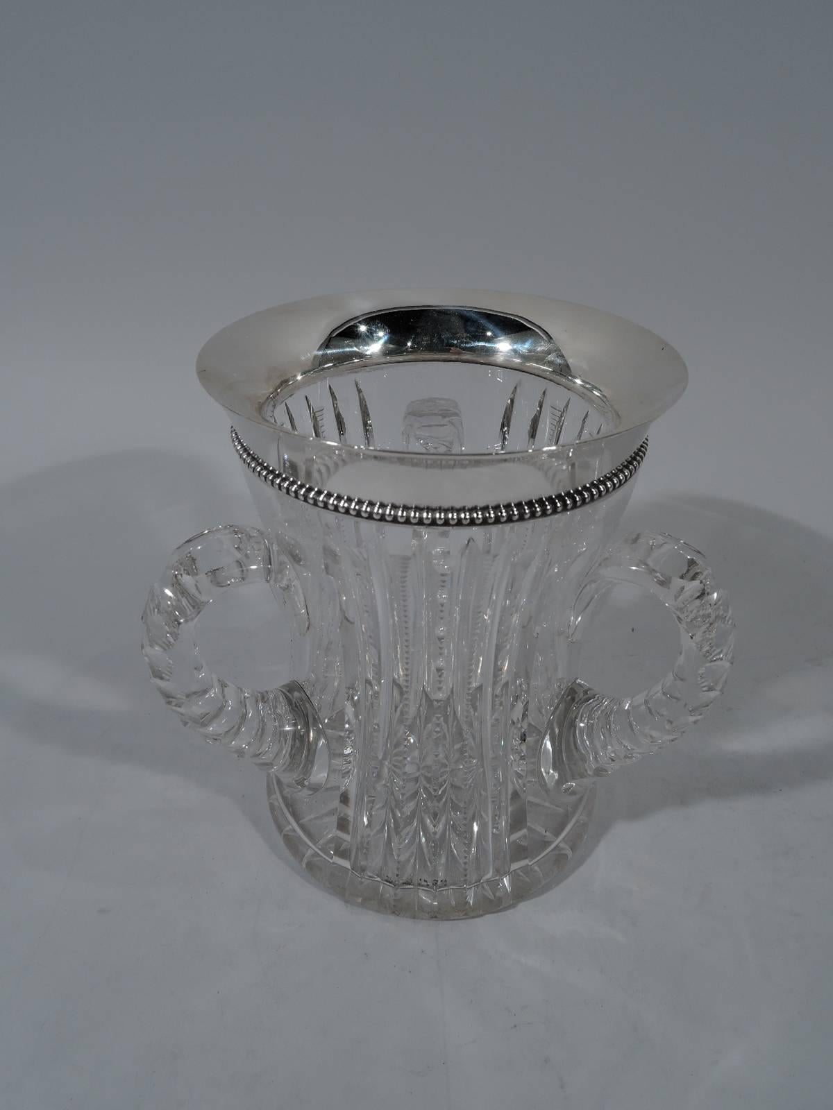 Brilliant-cut glass loving cup with sterling silver collar. Made by Wilcox (a division of International) in Meriden, Conn., circa 1900. Concave cylinder with 3 c-scroll handles. Notched flutes and facets. Flared collar with beaded rim. Hallmarked.