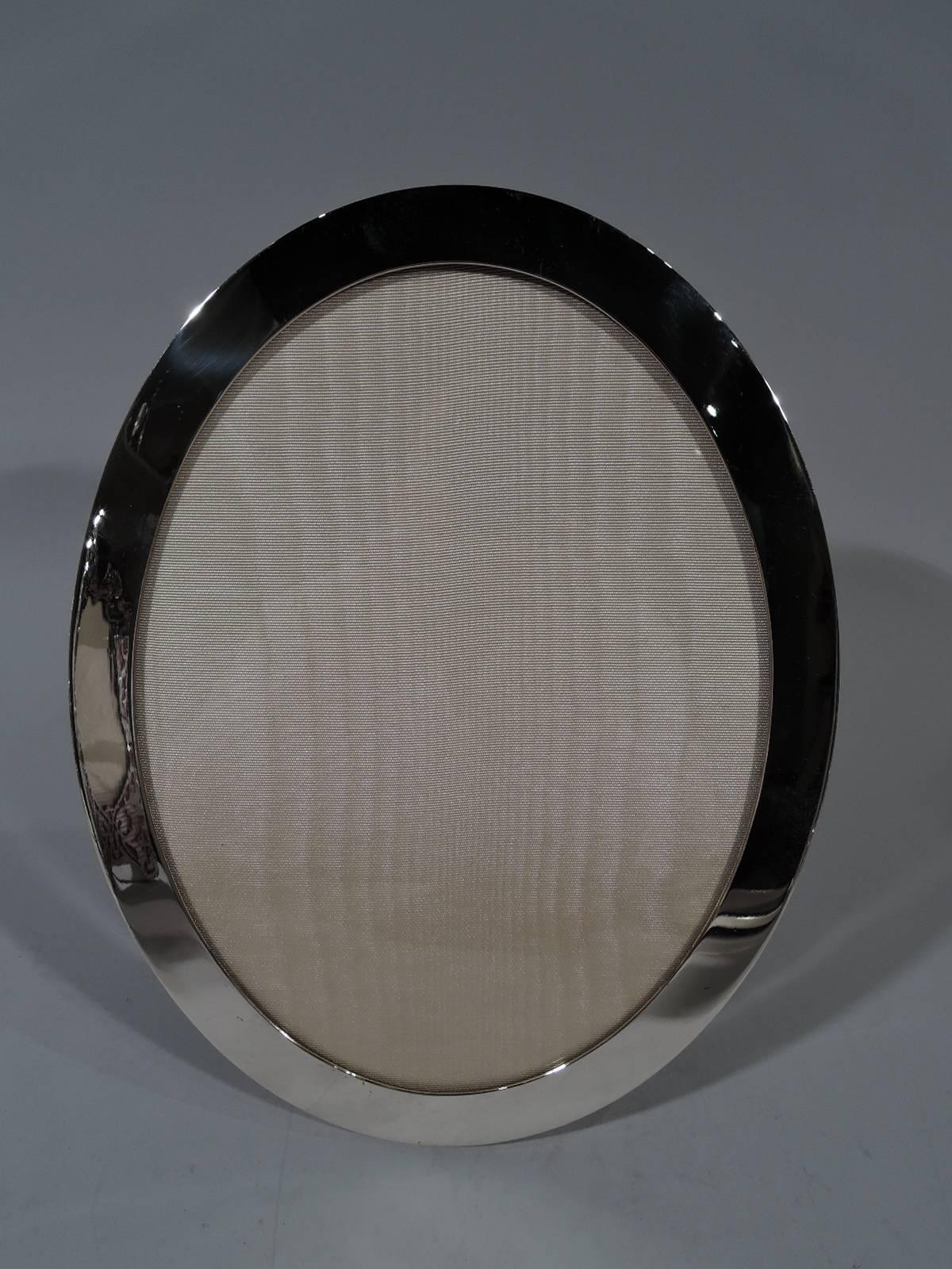 Modern sterling silver picture frame. Made by Tiffany & Co. in New York. Oval window with plain flat border. With glass, silk lining, and stained-wood back and hinged support. Hallmark includes postwar pattern no. 25033.

Dimensions: Frame: H 11 x