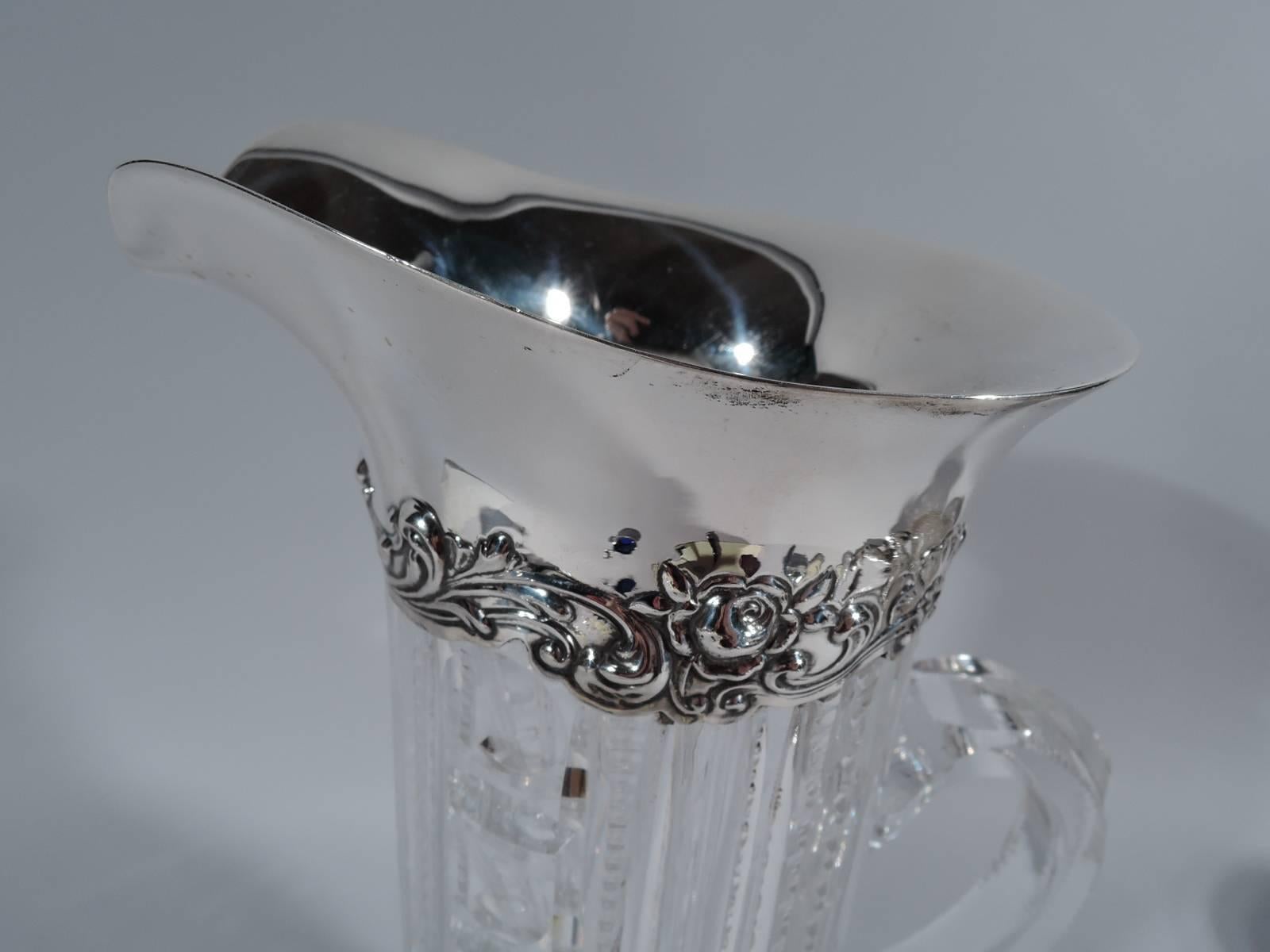 Lovely cut-glass claret jug with sterling silver collar. Made by Gorham in Providence, ca 1910. Cylindrical with C-scroll handle and spread base. Vertical ornament, including flutes, notches, and abstract egg and dart. Collar has helmet mouth and is