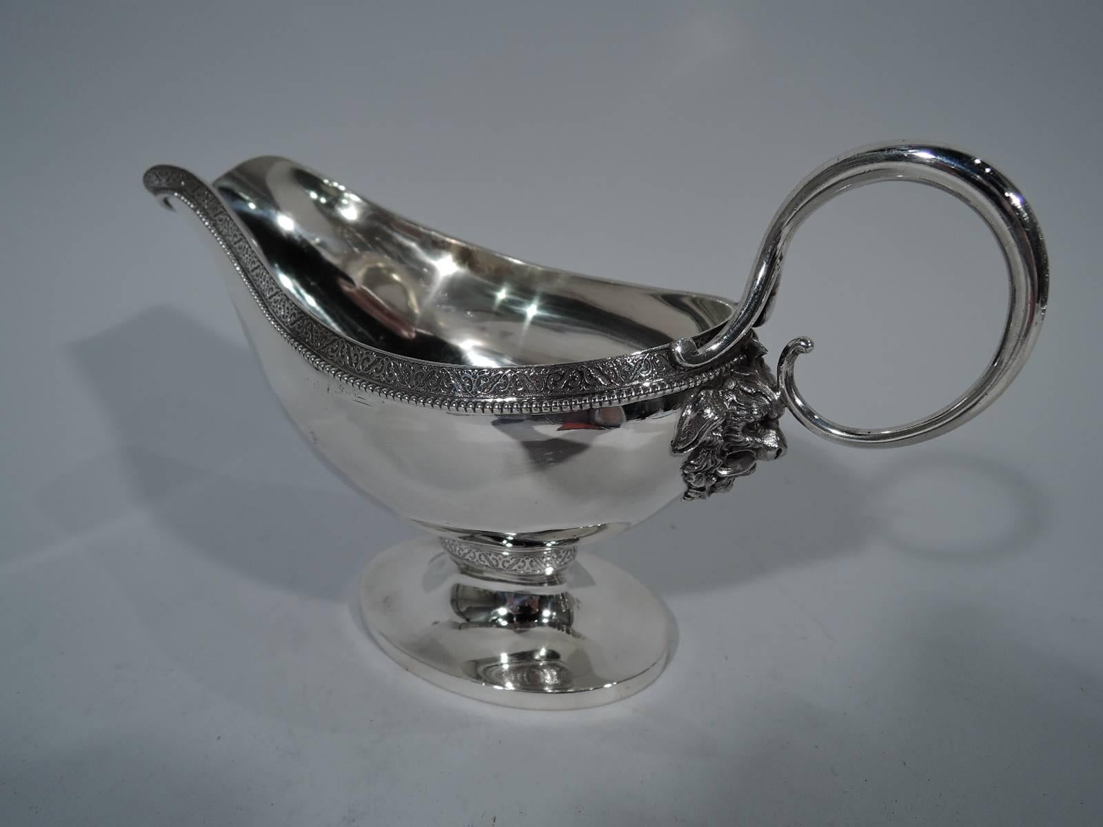 Classical sterling silver gravy boat. Made by Gorham in Providence in 1871. Curved body with helmet mouth, raised oval foot, and loop handle with mask mount. Raised rinceaux on stippled ground and beading. Hallmark includes date letter and no. 112.