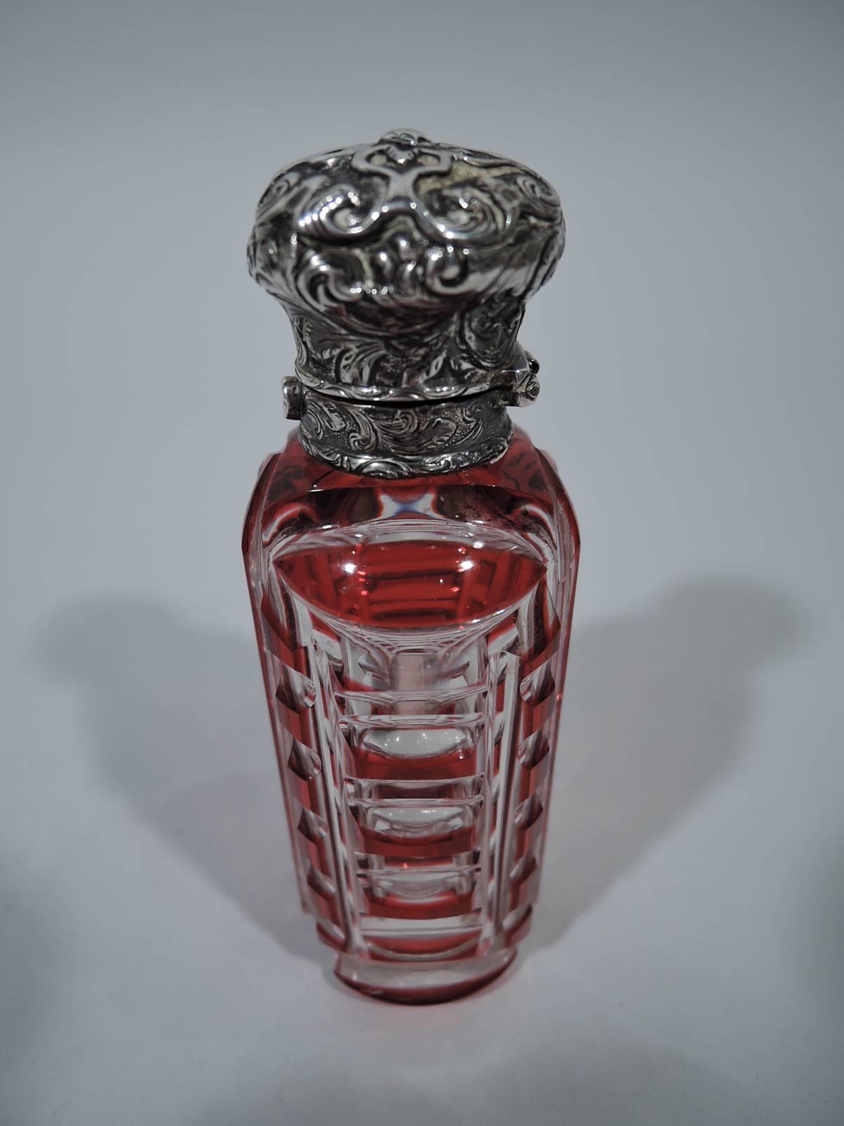 European silver and cut-to-clear red glass perfume, circa 1880. Ovoid bottle with cut geometric ornament. Silver collar and hinged bun cover with worked scrolls. Tactile and eclectic. Unmarked.